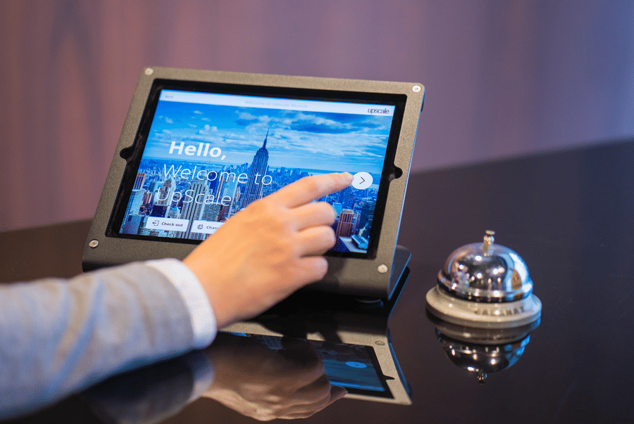 Hand tapping a check-in tablet beside a service bell on a desk
