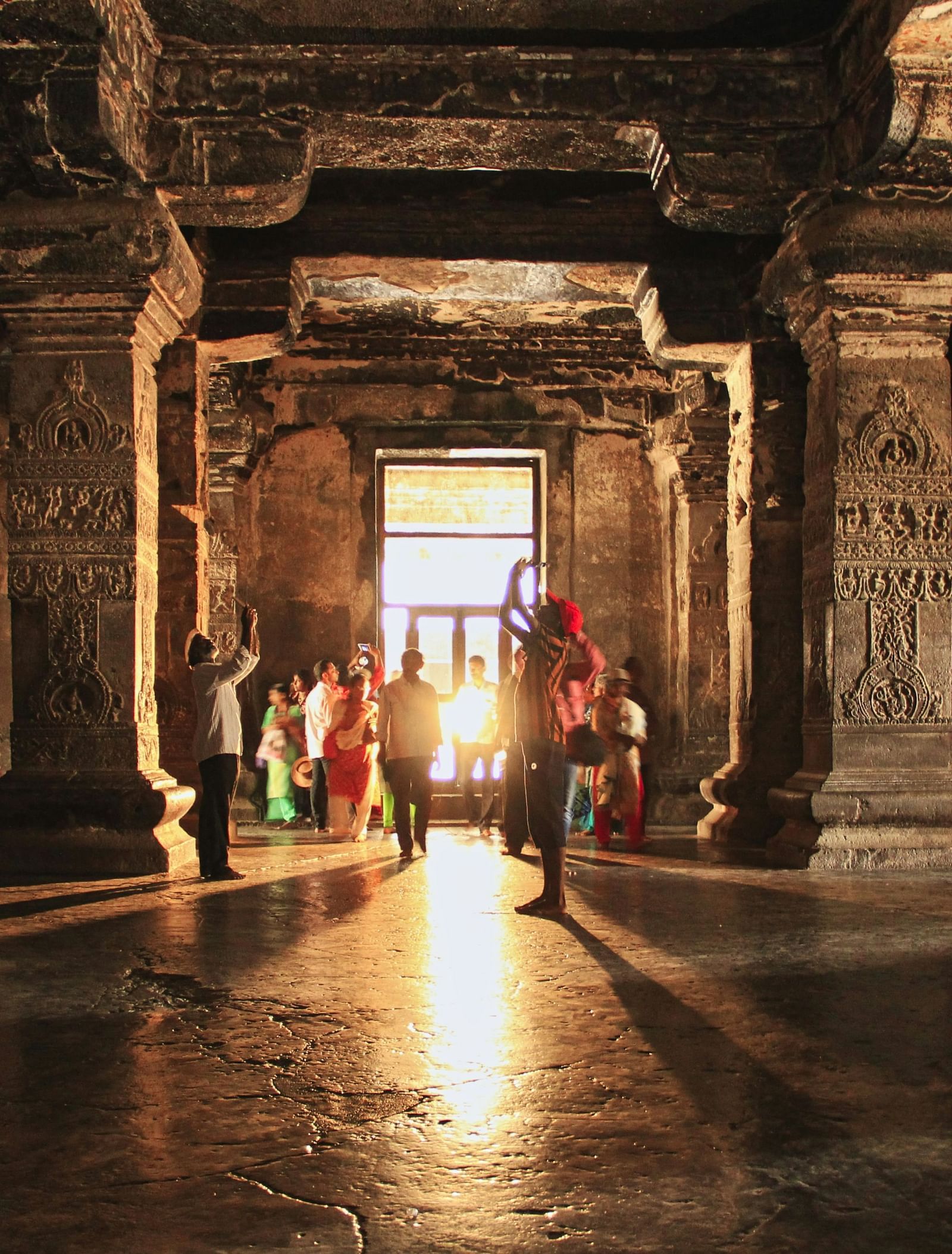 image of a cave with many tourists glancing through the intricate stone pillars with a golden beam of sunlight entering the cave from behind