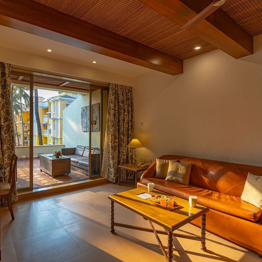 A living room that includes a sofa, coffee table, tea and coffee maker, a TV, and an outdoor balcony with seating arrangements.