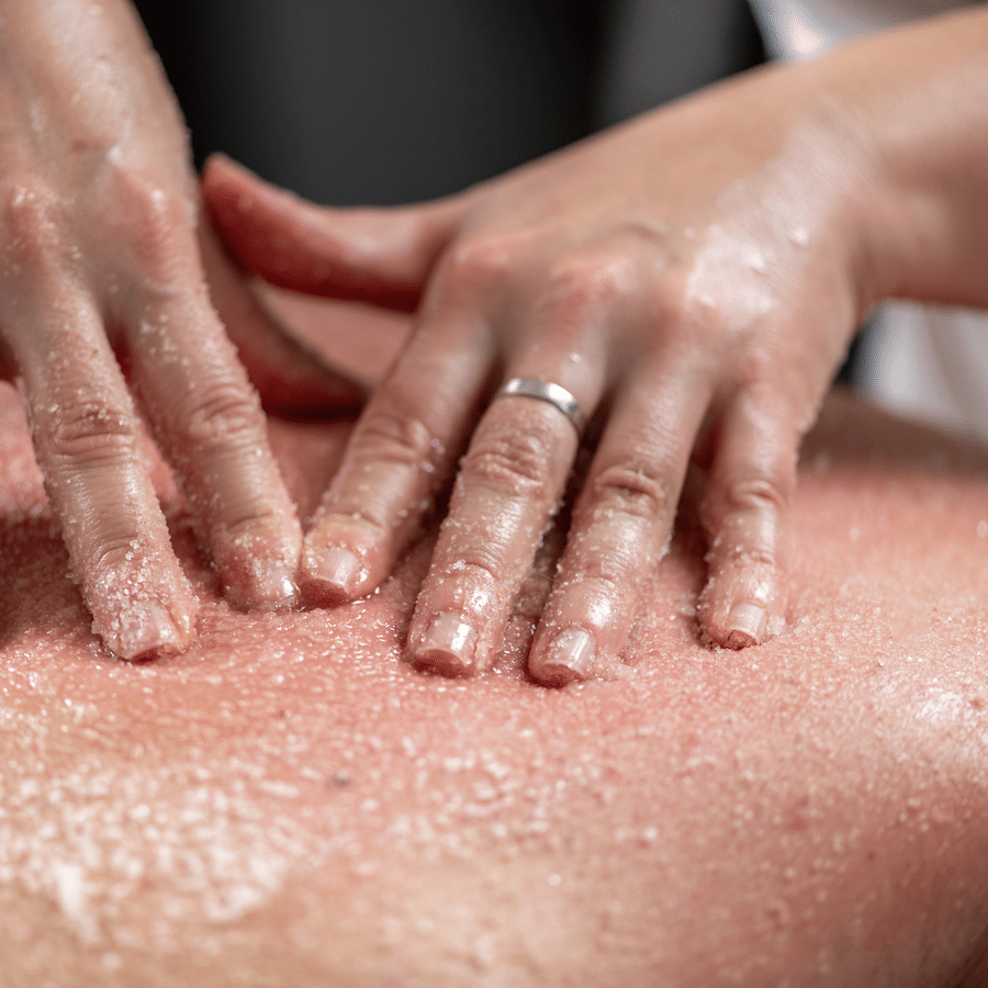 Therapist exfoliating a client's back using a scrub during a body treatment.