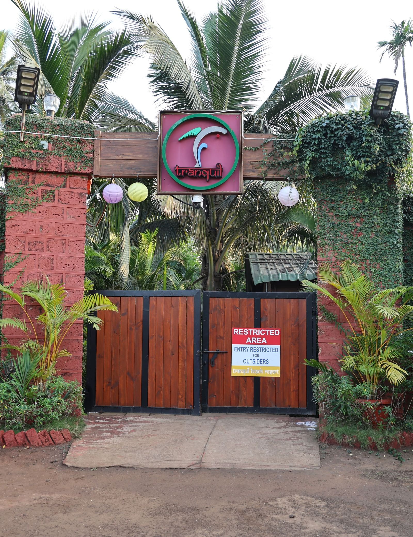 Ornate resort entrance gate made of stone and wood, surrounded by lush green foliage - Tranquil Beach Resort, Harihareshwar