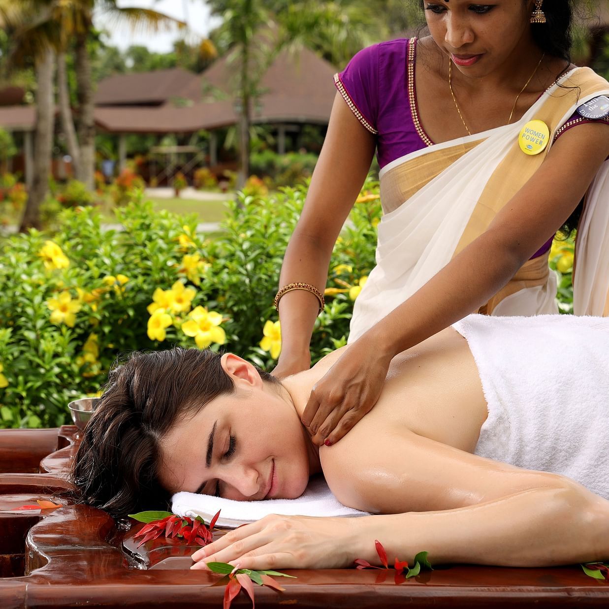 A woman receiving a relaxing neck and shoulder massage while lying on her stomach outdoors at Ayurveda Spa, Uday Backwater Resort