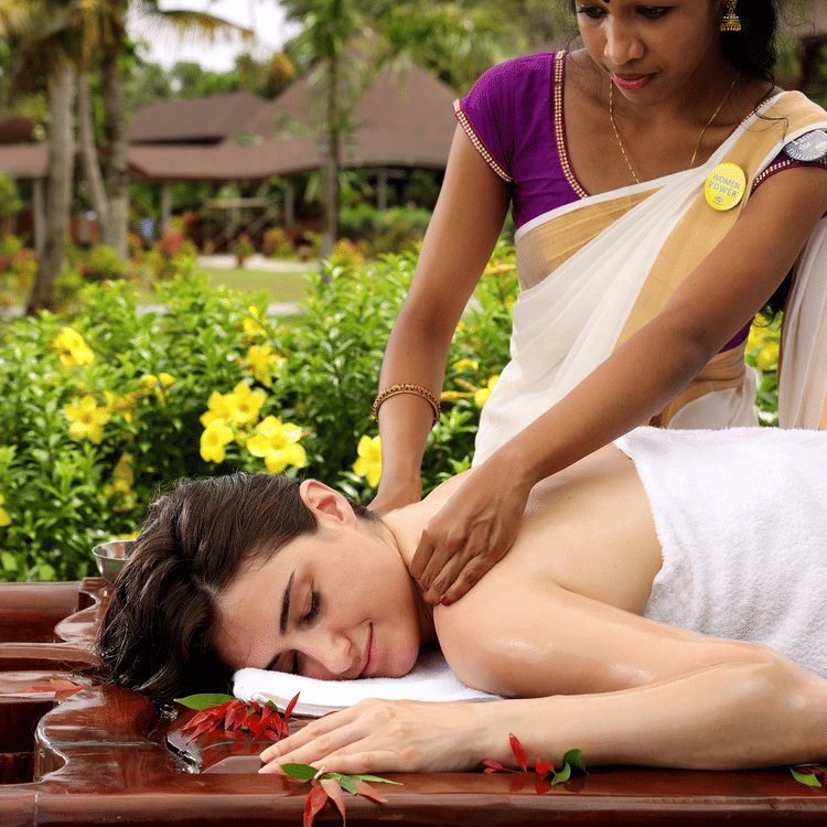 A woman receiving a relaxing neck and shoulder massage while lying on her stomach outdoors at Ayurveda Spa, Uday Backwater Resort