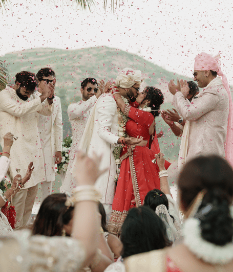Bride and groom celebrating with family and guests beneath a shower of flower petals overlooking Bagela Lake | YAAN Udaipur