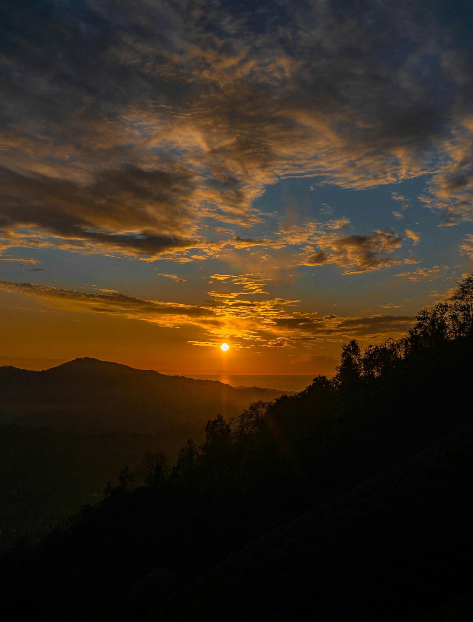 A silhouetted view of a valley with the sun setting in the background.