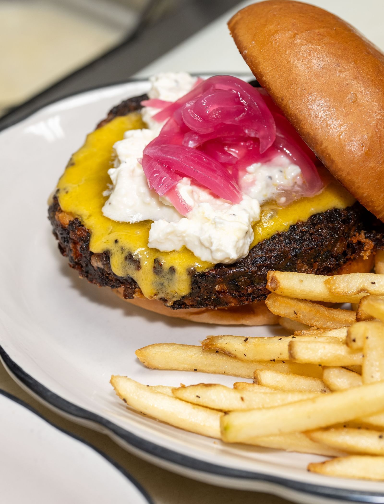A juicy gourmet burger topped with cheese and red onions, served with crispy golden fries at The Tallman Hotel.