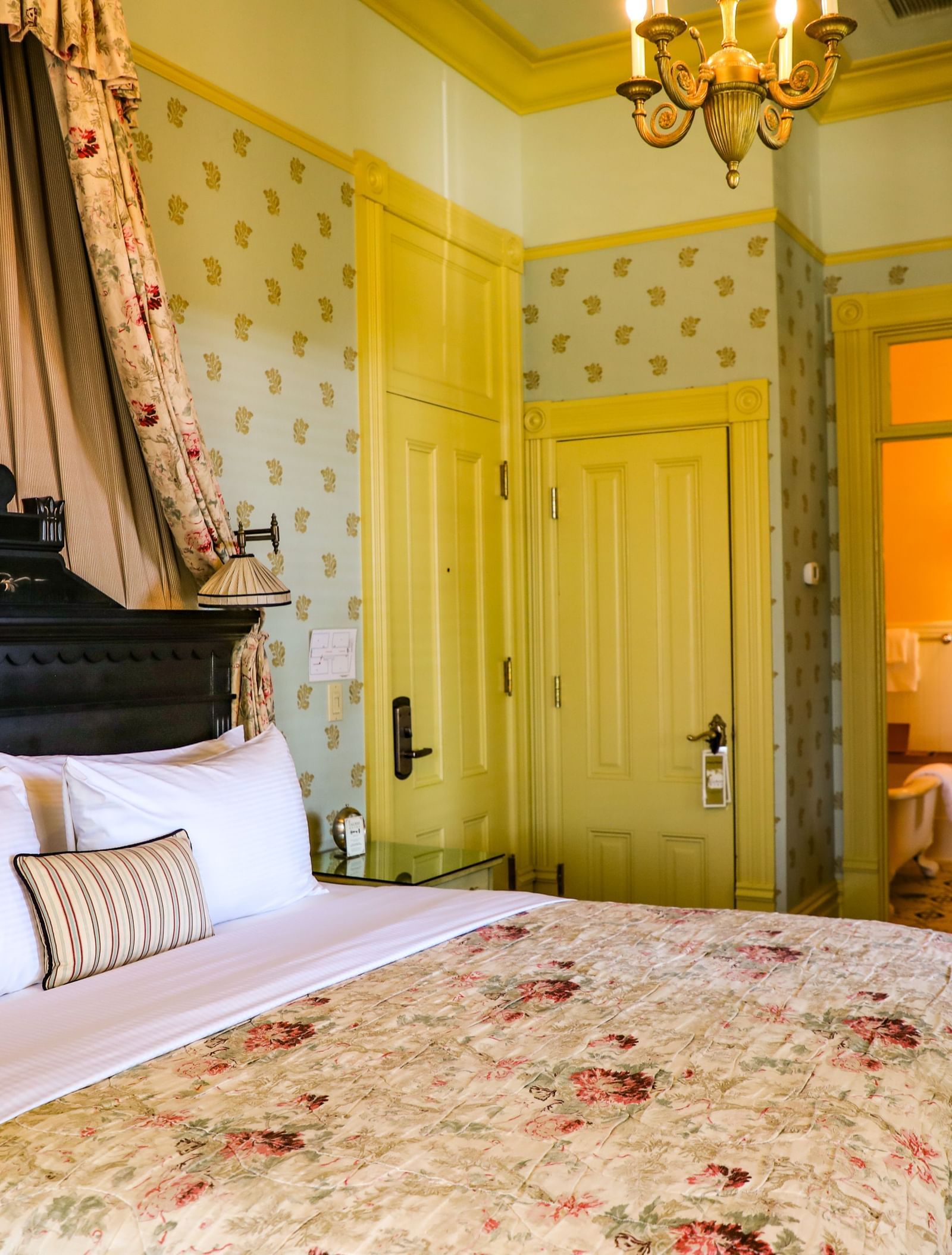 A lavish Tallman Hotel guest room features a four-poster bed with floral drapes and bedding, and elegant yellow wallpaper.