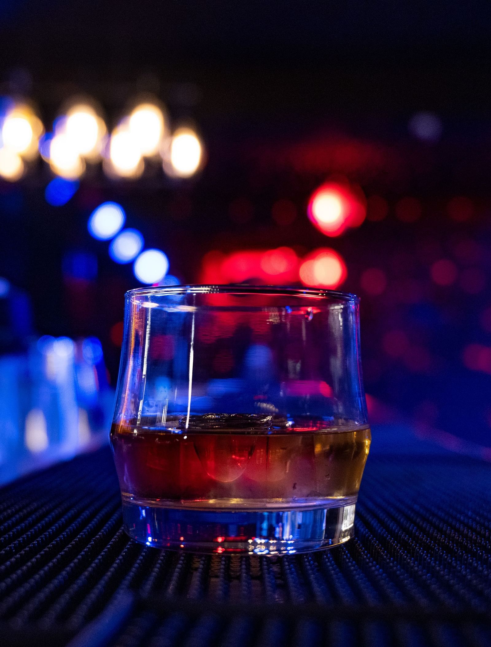 a close up image of a glass holding whisky in a dimly lit bar counter at the bourbon club and lounge - The Tattva Boutique Resort