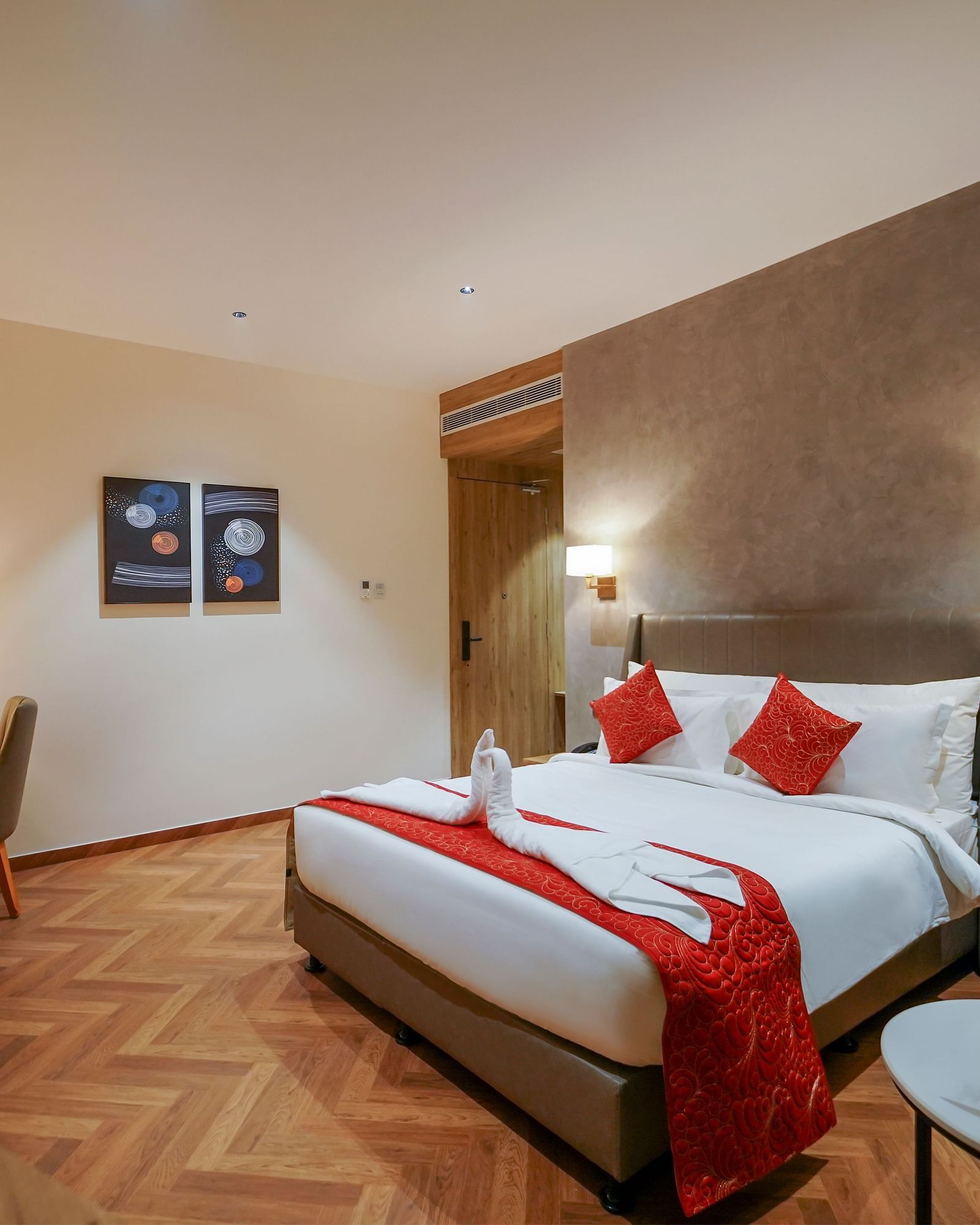 A hotel room offers a bed with decorative towels and pillows, a desk with a chair, and a small round table with flowers - Hotel Park Inn, Nellore.