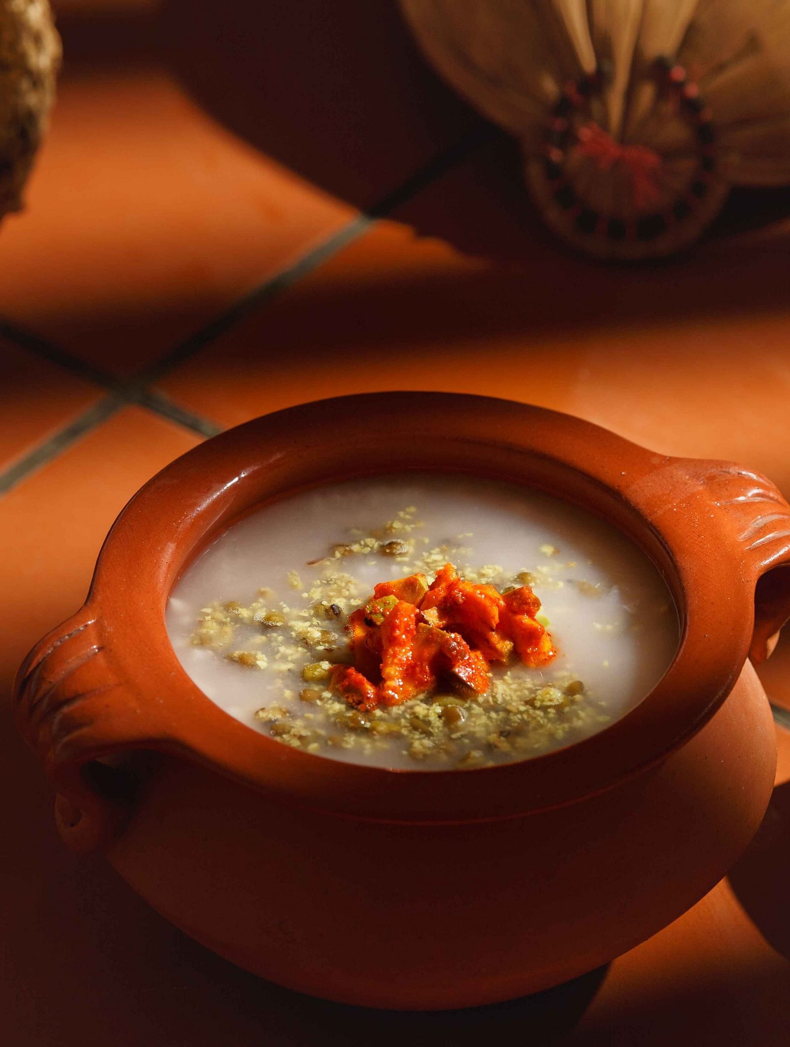 A close-up of a clay pot filled with a creamy dish, garnished with spices and herbs.