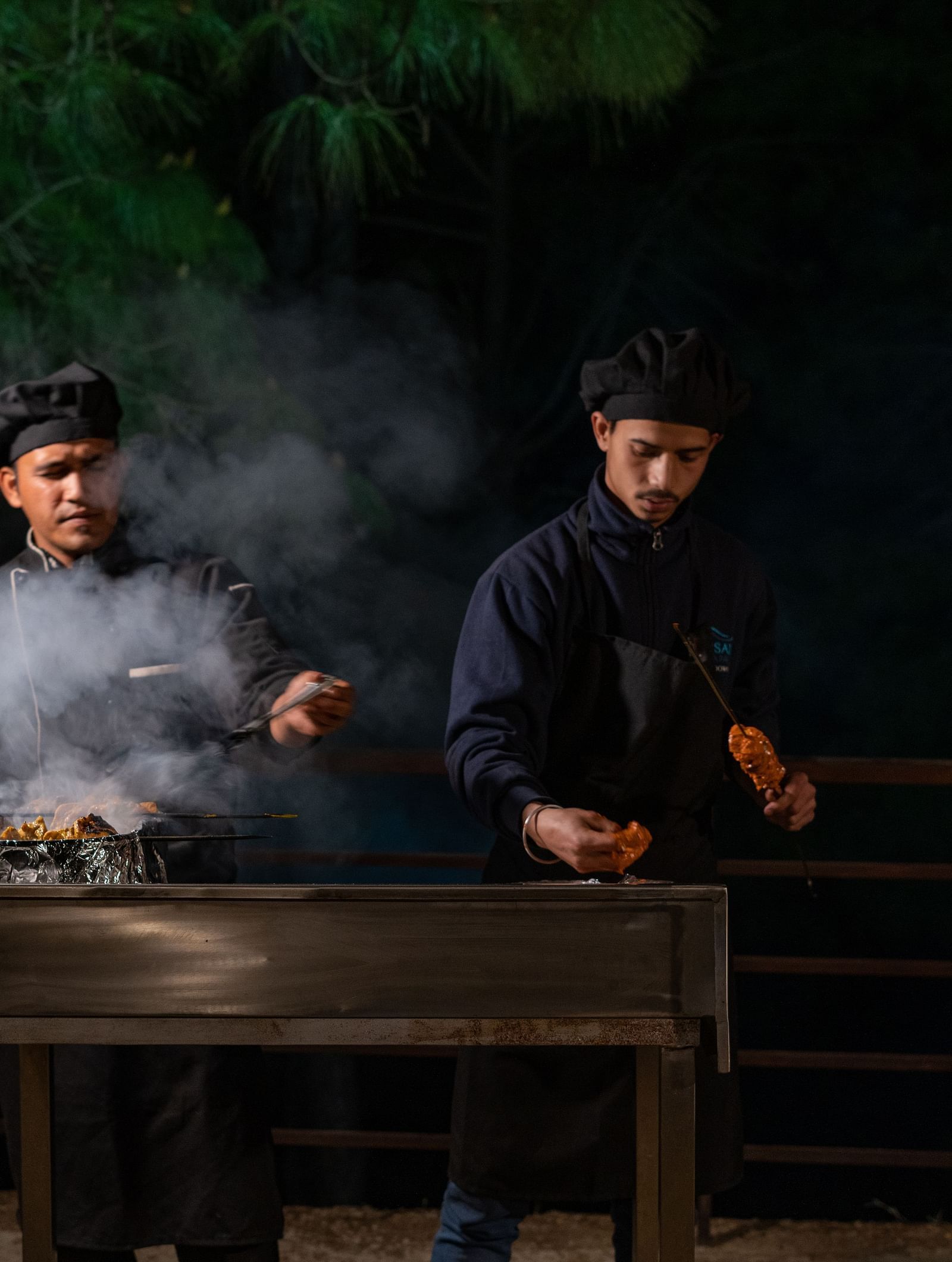 Two chefs preparing barbecues with smoke rising from the sizzling grills at BluSalzz Escapade Resort, Lansdowne