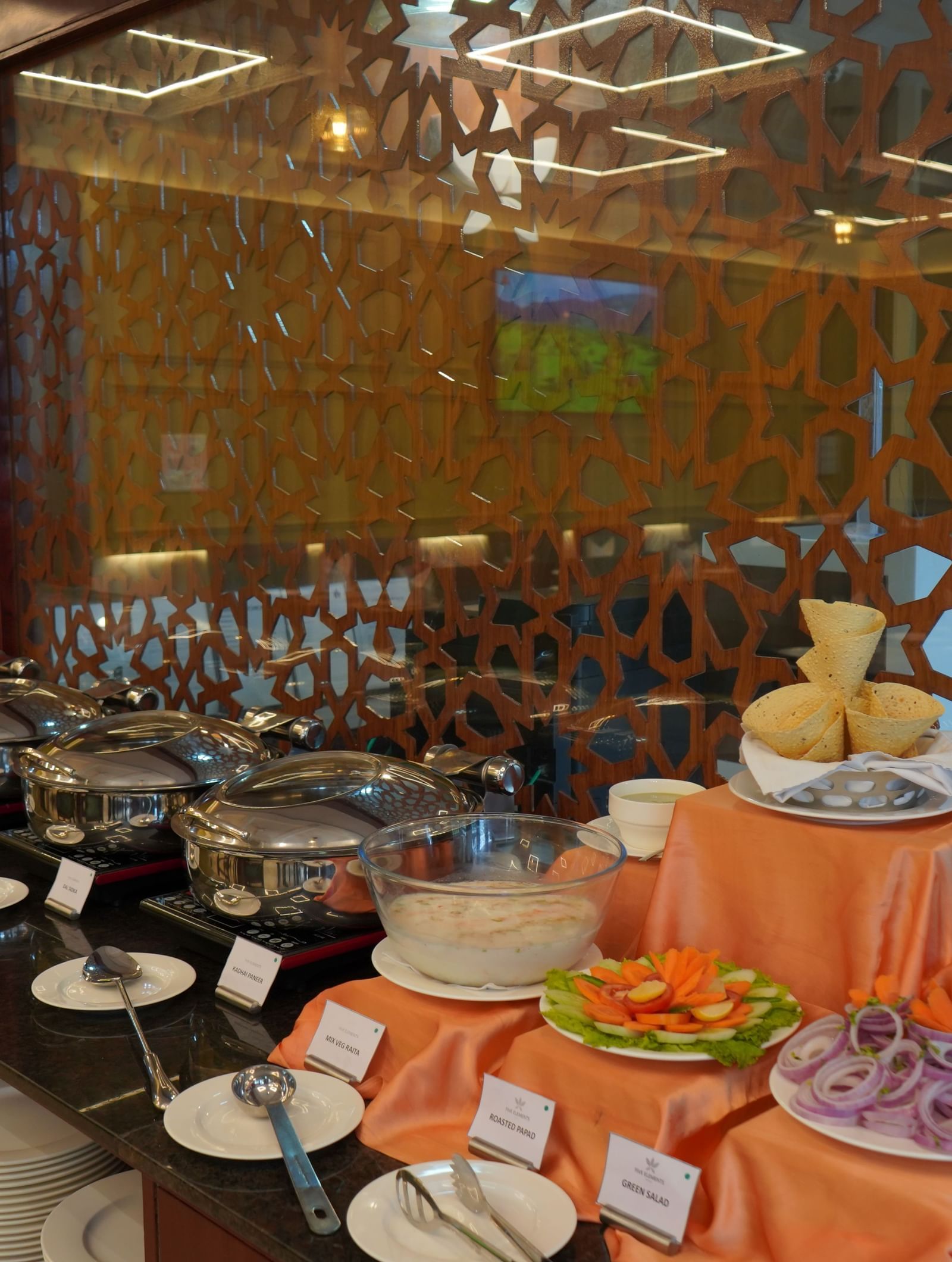 A wide shot of a buffet table with a variety of serving dishes. The background has a decorative wooden screen.