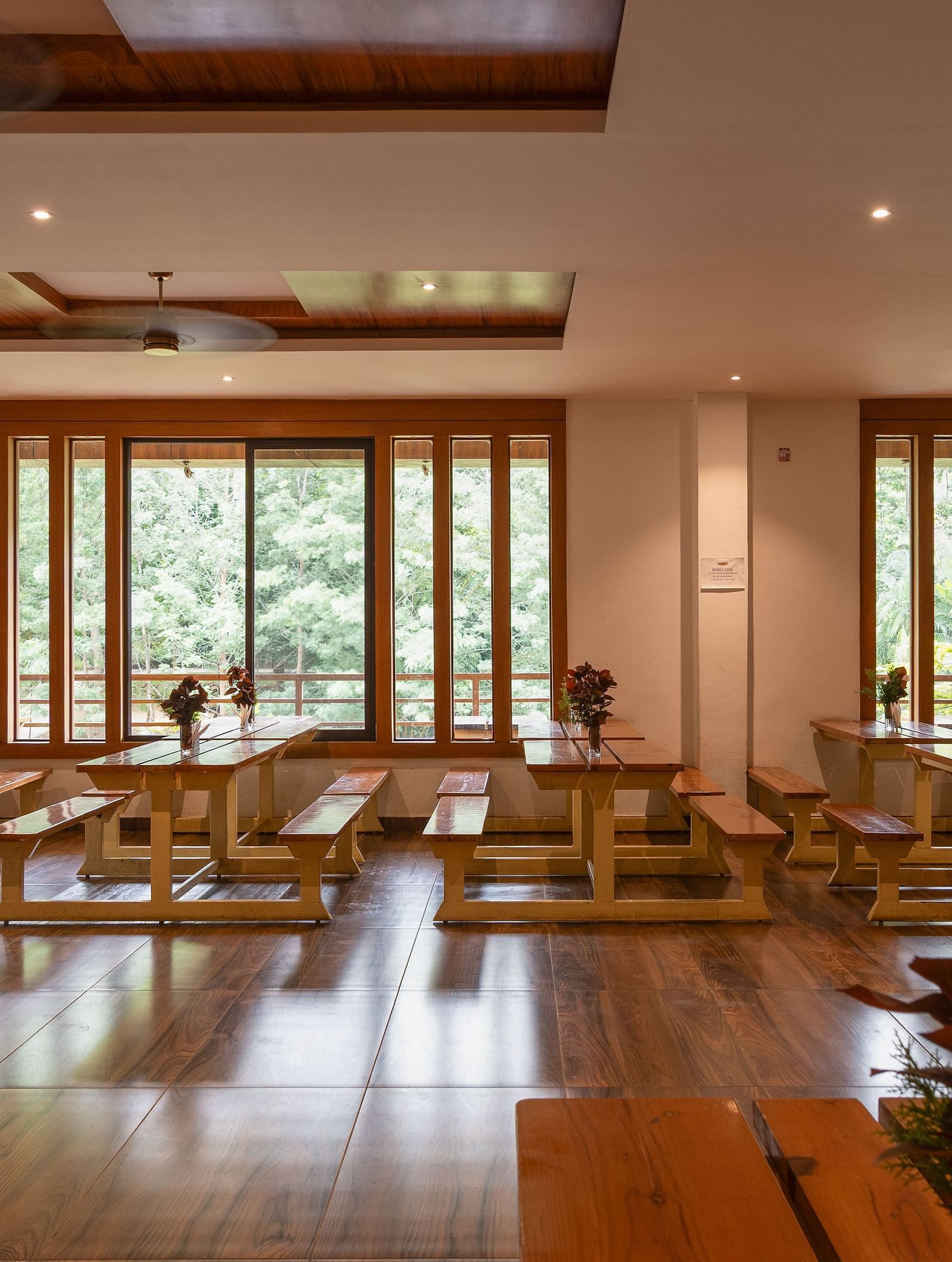 A spacious dining hall with wooden floors and high ceilings offers multiple tables and chairs, with large glass doors opening to an outdoor area | Lake View Restaurant