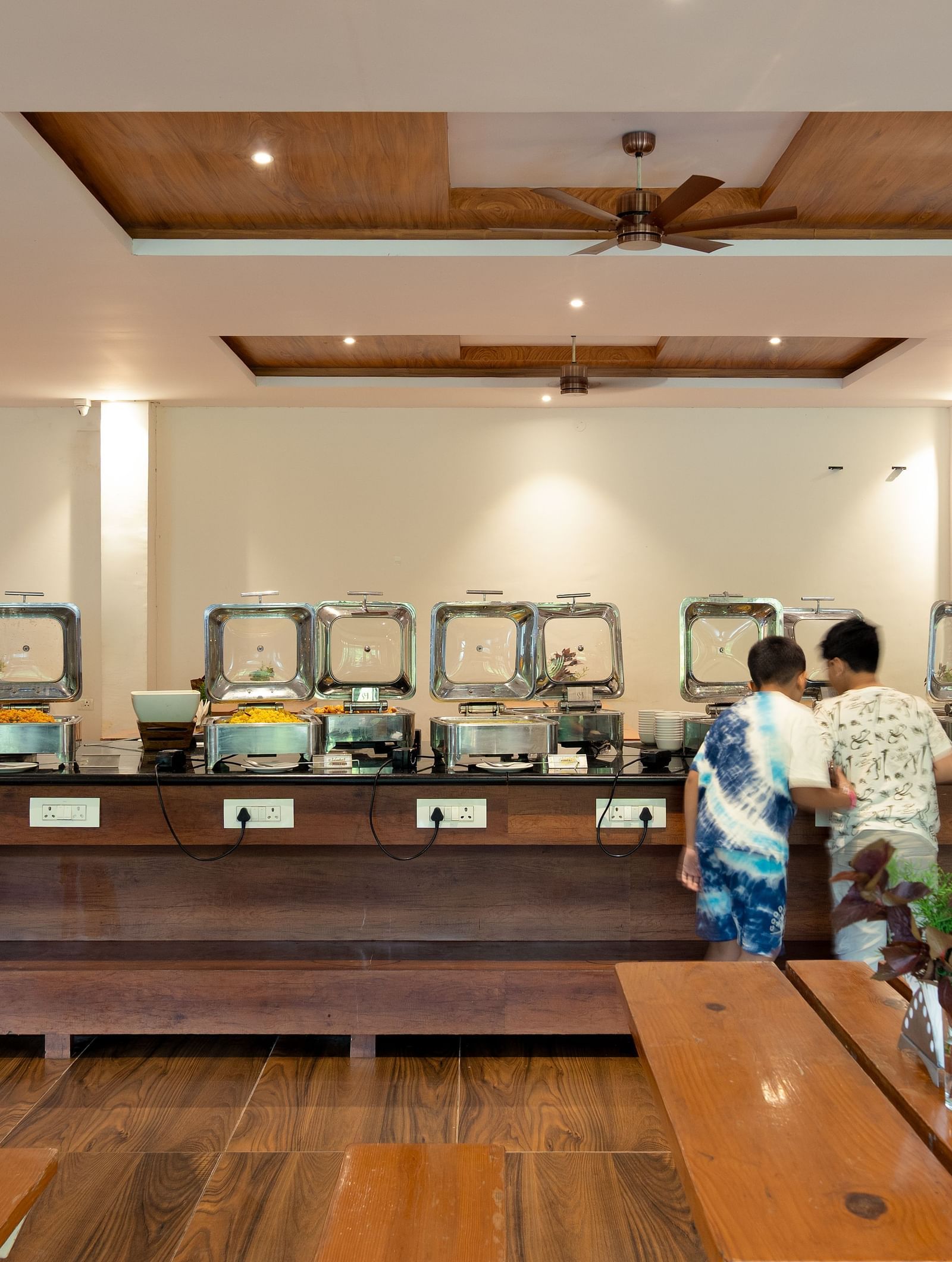 A well-lit indoor dining area features a buffet setup with multiple food warmers and a few people present | Lake View Restaurant