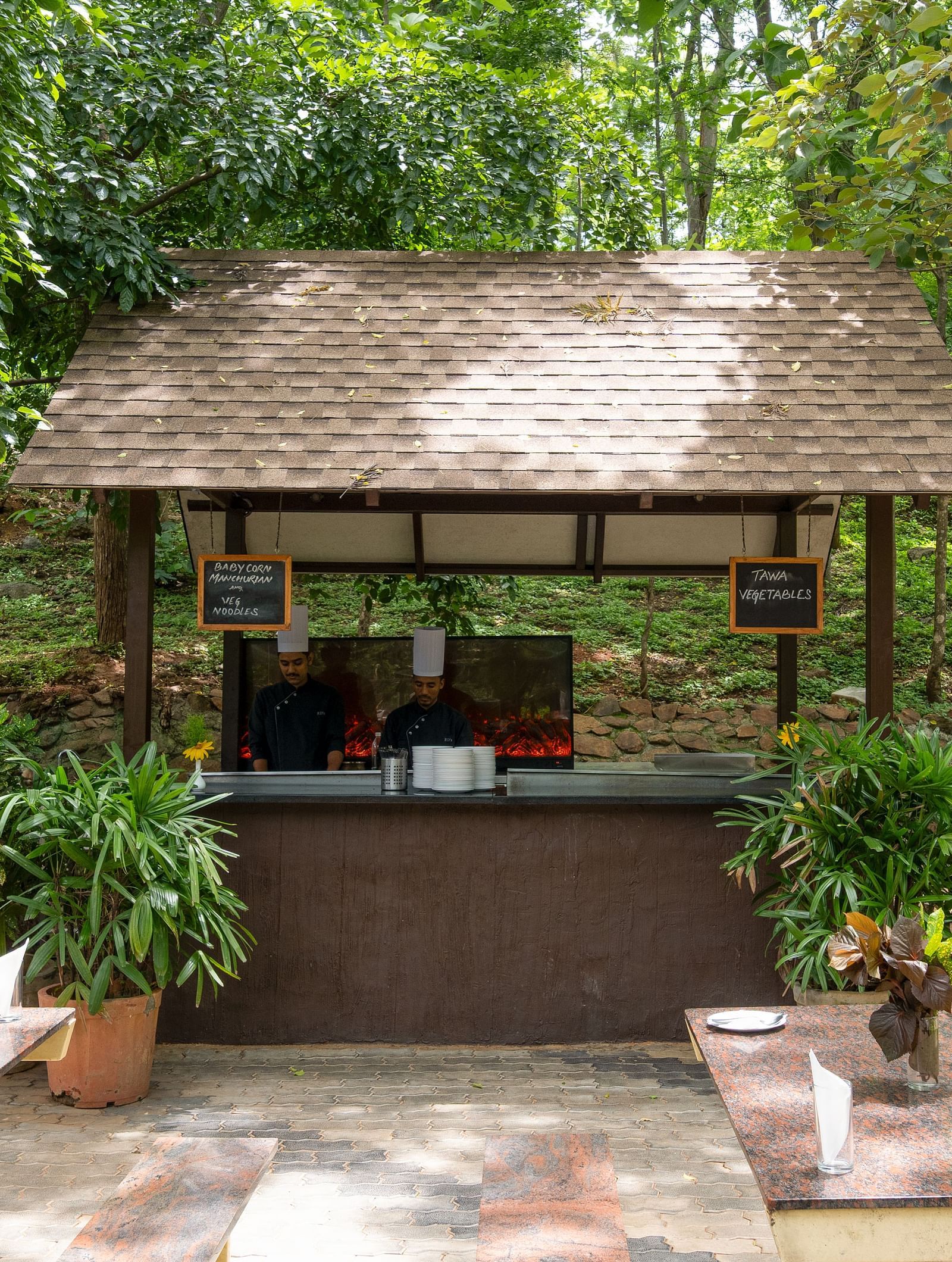An outdoor service counter with a thatched roof sits amidst trees and greenery, offering a shaded spot for refreshments | Lake View Restaurant