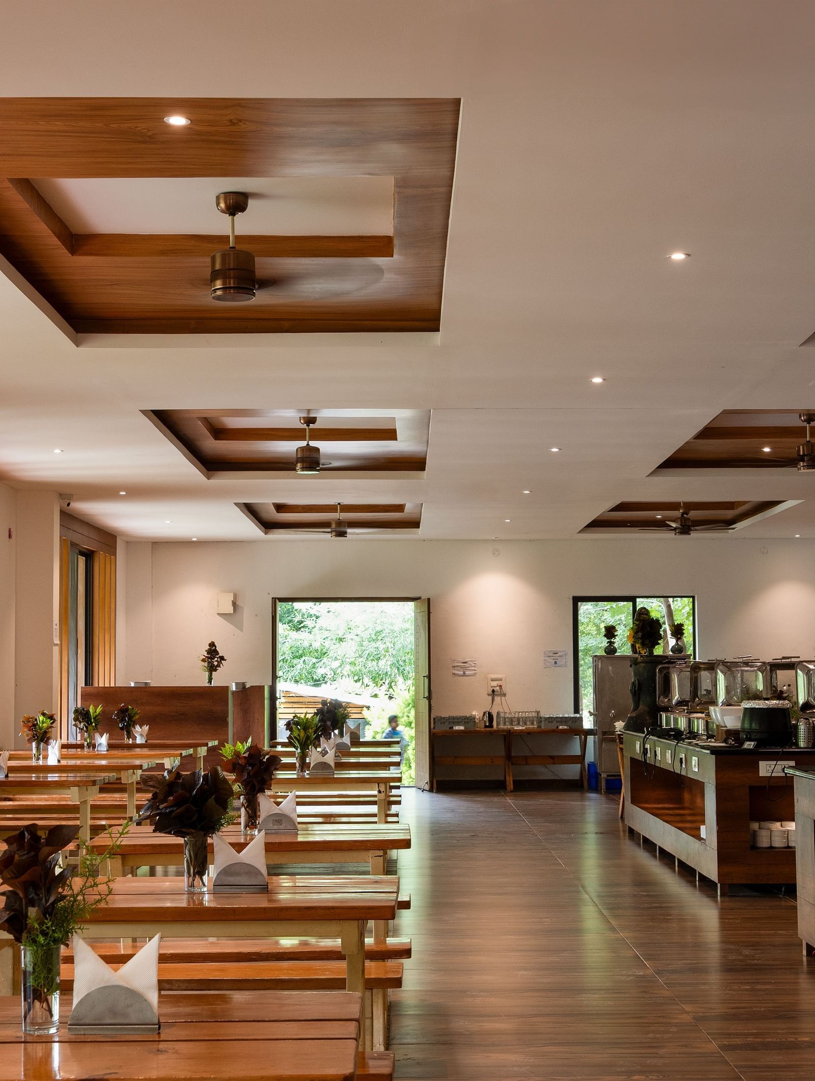 A well-lit restaurant interior features a buffet line on the left and dining tables with chairs on the right, all under a decorative wooden ceiling | Lake View Restaurant