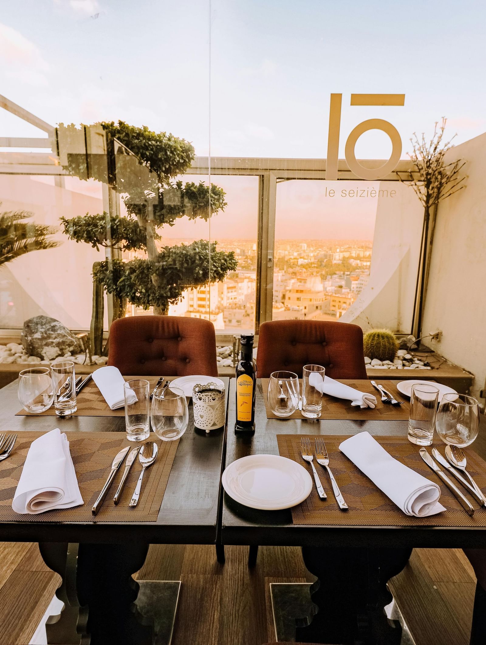 A well-arranged dining table with cutlery and glassware featuring mesmerising city views in the background beyond the glass panels on the terrace.