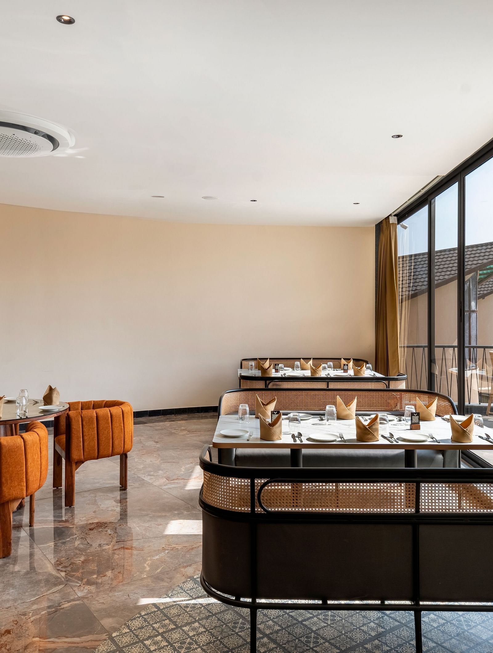 Fine Dine with warm lighting, featuring wooden tables and chairs, a comfortable sofa, and large windows offering a view of the outside at The Qualia Resort Club & Brewery, Udaipur.