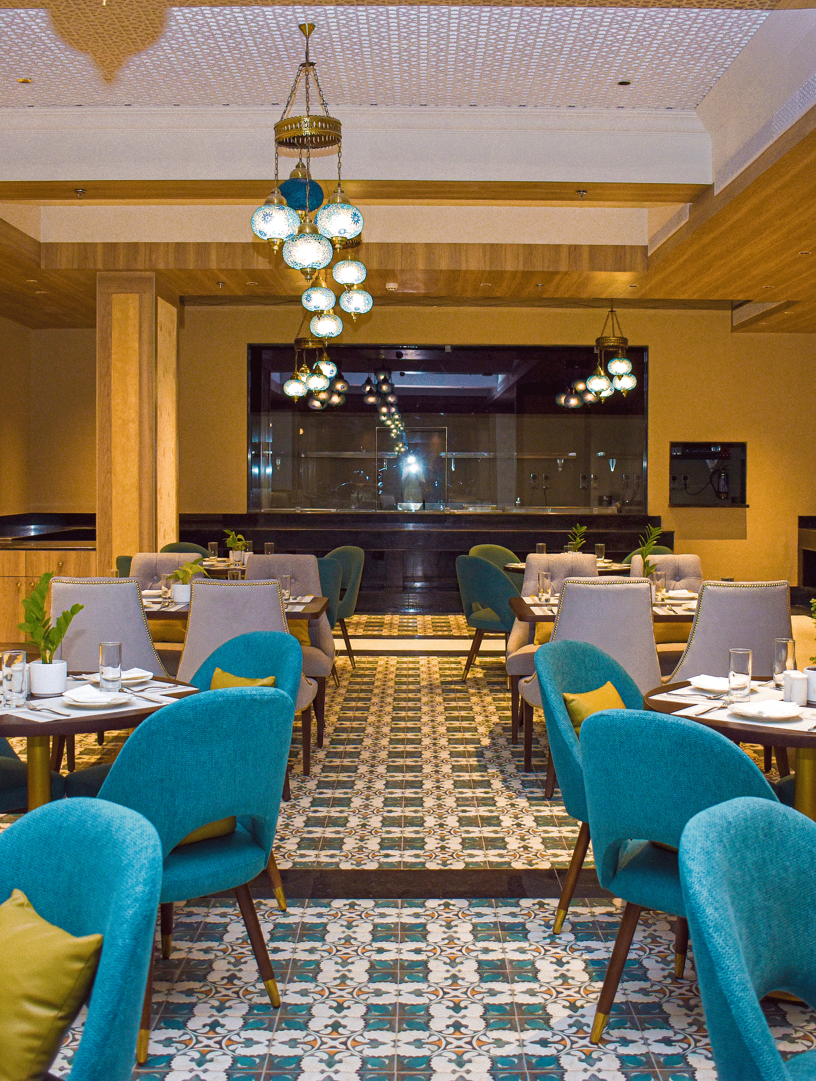 A modern restaurant interior with teal armchairs, round tables, patterned tile floor, and a distinctive globe chandelier - Urban Suites by BluSalzz, Jaipur