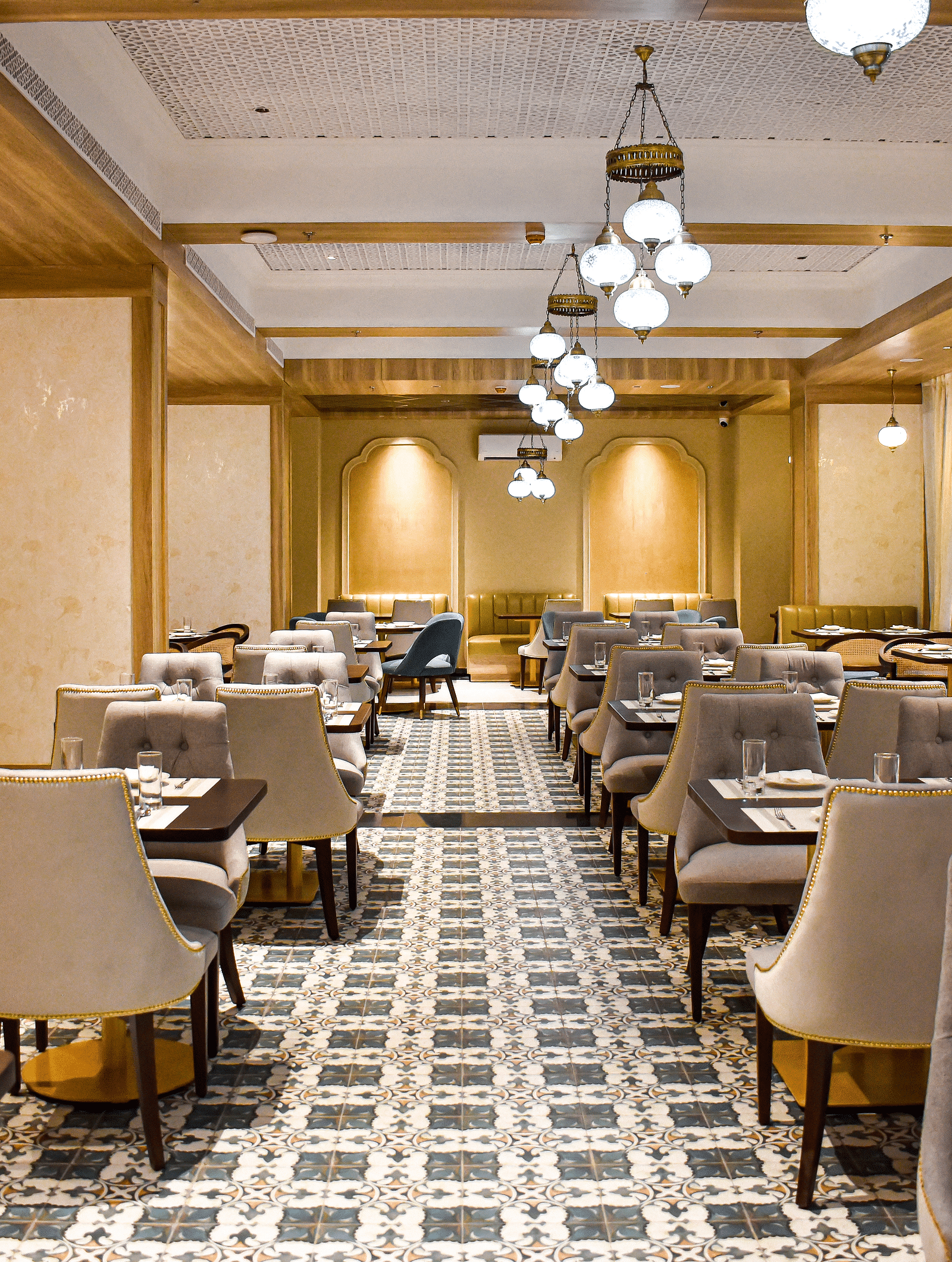 A restaurant interior with patterned tile floor, upholstered chairs, set tables, hanging pendant lights, and decorative ceiling panels - Urban Suites by BluSalzz, Jaipur