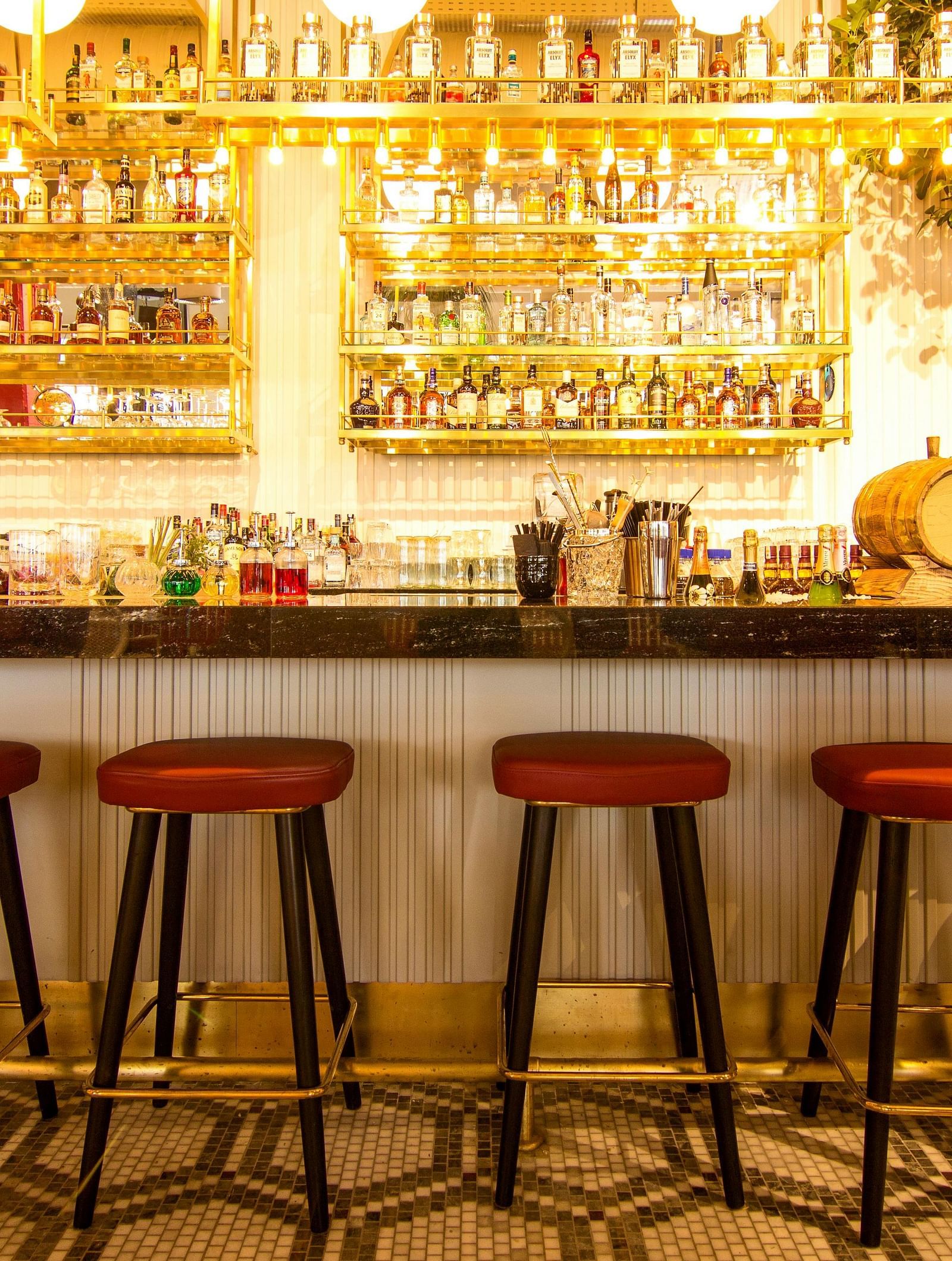 A bar with red stools lined up in front of a well-stocked back bar with bottles and glasses.