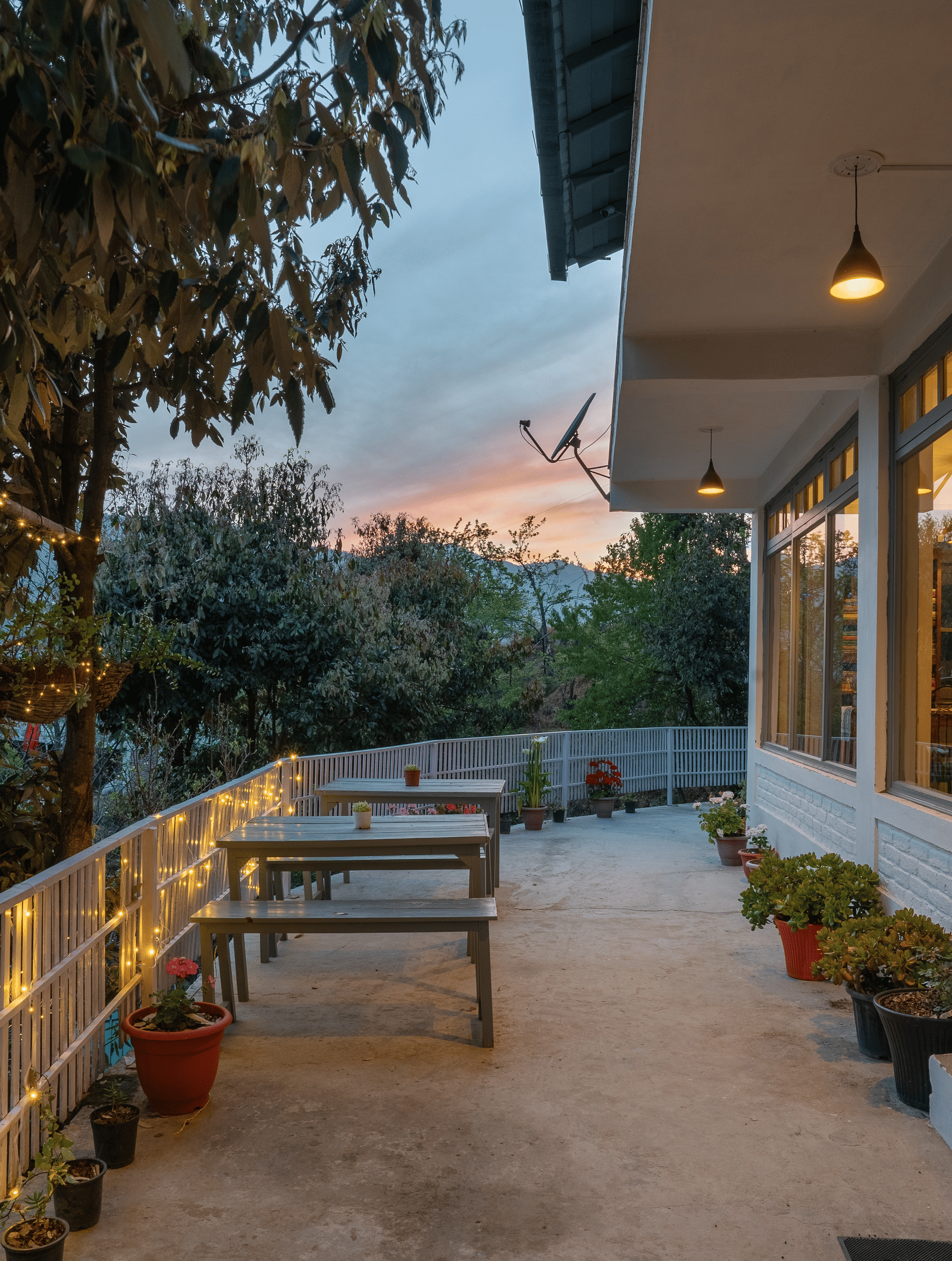 An outdoor shot of the Ziran Retreat terrace area at dusk, with wooden benches and tables and lighting on the walls, overlooking a scenic view.