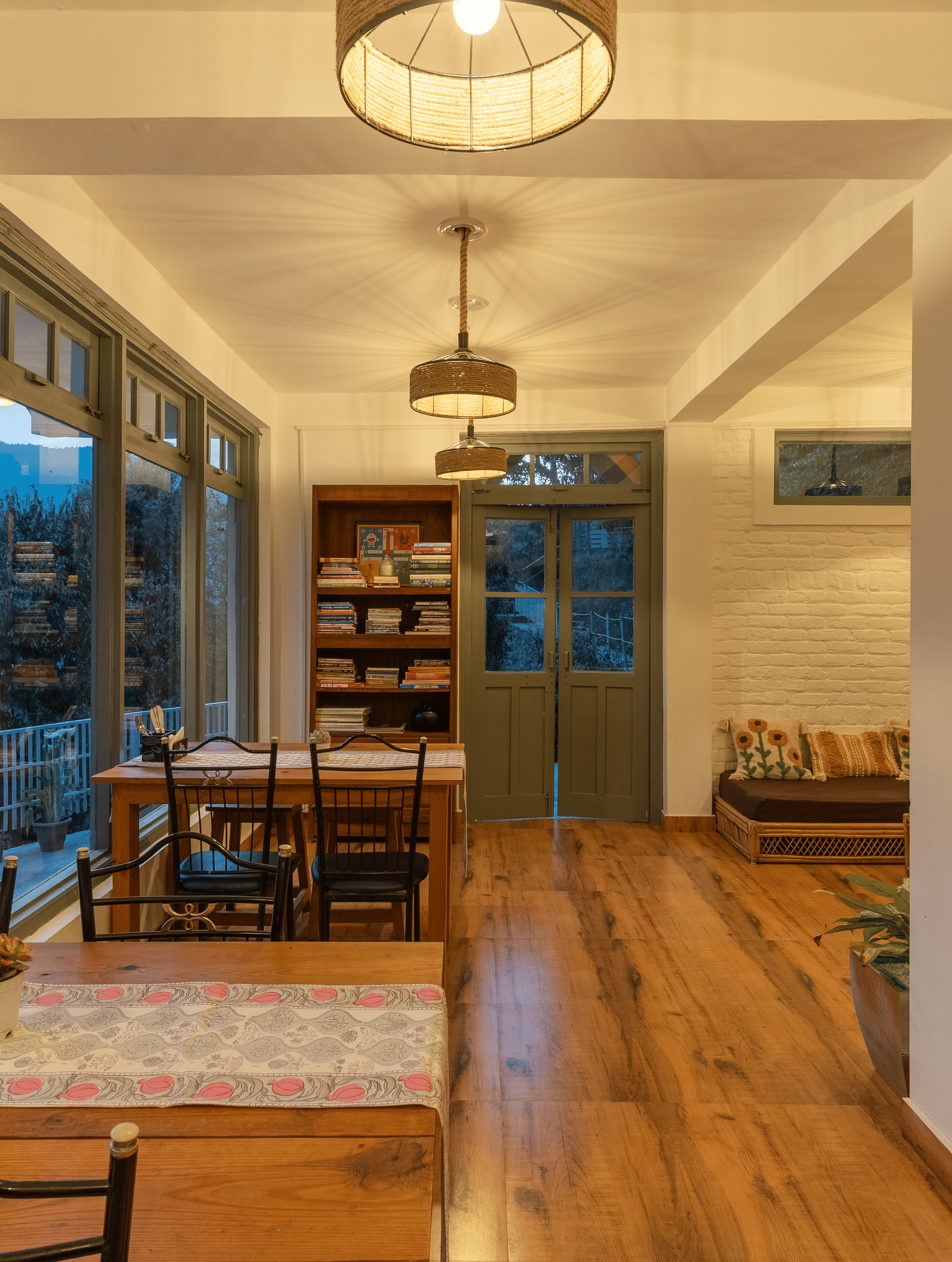 A wide shot of Ziran Retreat's main room, showing a living area with a sofa, a dining area with a table and chairs, and large windows looking out at the scenery.