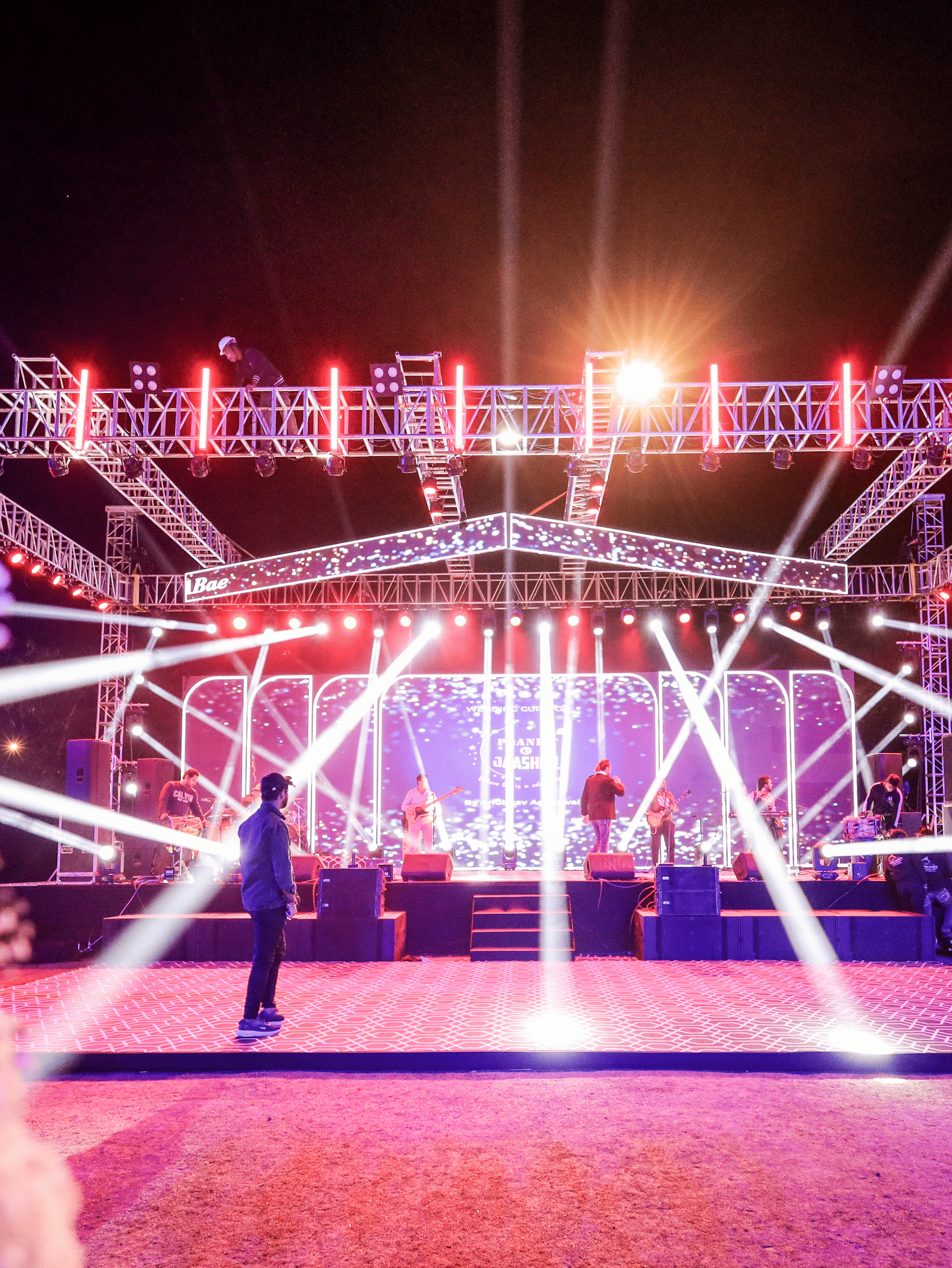 A large, brightly lit performance stage at Ananta Spa & Resort, Jaipur, is surrounded by white floral decorations in the foreground.