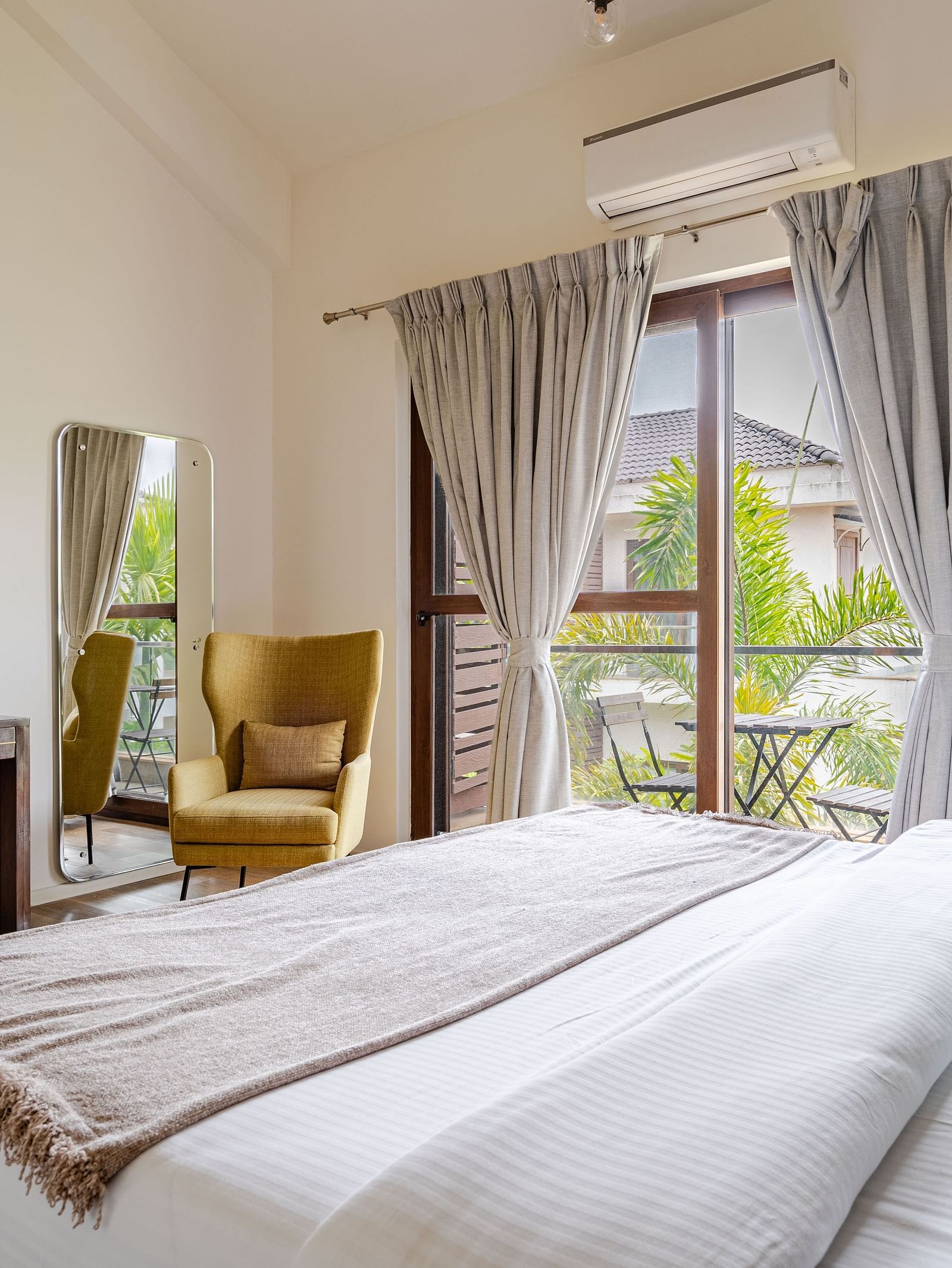 A bedroom at Lindsay Manor featuring a double bed, desk, cushioned chair, wall art, and a large window with curtains.