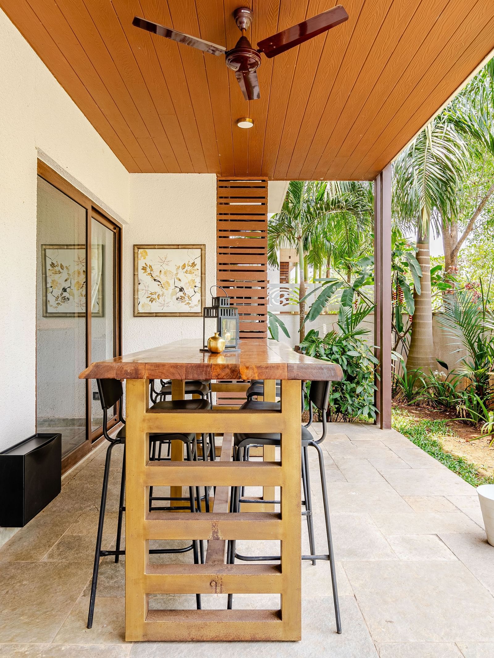 Covered outdoor dining space with a live-edge wooden countertop, high stools, ceiling fan, and lush garden surroundings offering a serene tropical vibe - Lindsay Manor
