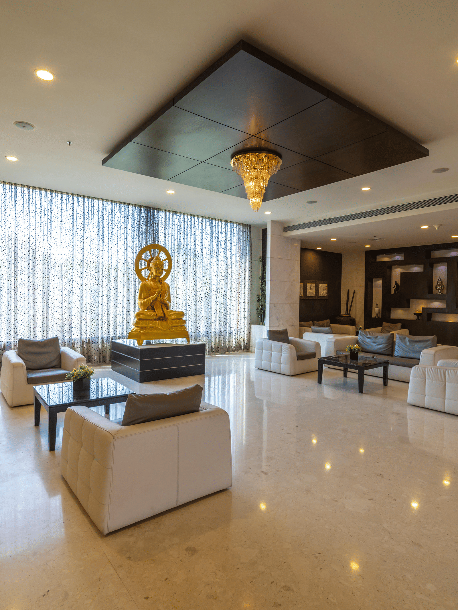 Hotel lobby area with amble seating and warm lighting, and a statue of an idol in the centre at Narayani Heights Hotel & Resorts, Ahmedabad.