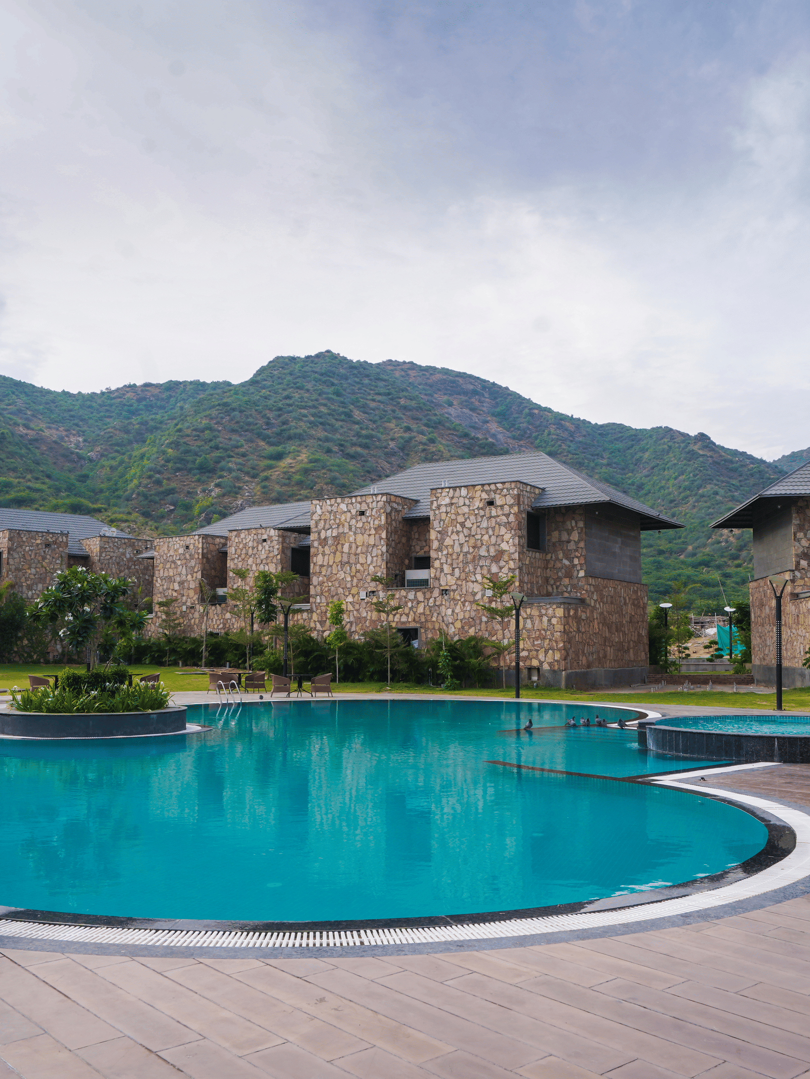 A swimming pool reflects the resort buildings. The surrounding area has view of several holiday villas with a view of the mountains.