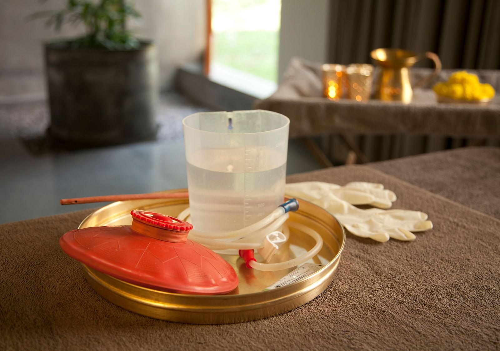 Gold tray with water glass, red flowers, white cloth, and small bowl on wooden table - Shreyas Retreat