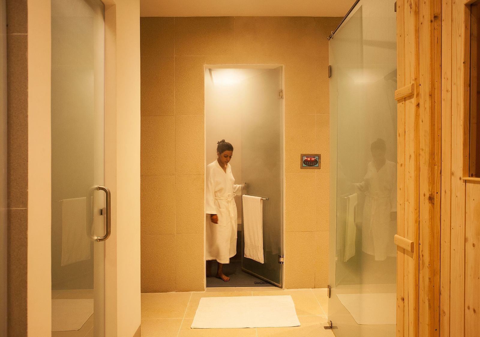 Person in a white robe standing in a shower, glass door, modern bathroom - Shreyas Retreat