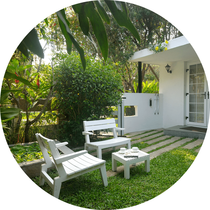 White outdoor seating arrangement in a garden with lush plants and a walking path at Amanvana Spa Resort, Coorg - Luxury Resort