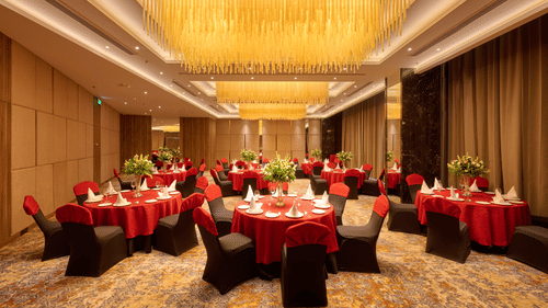 A large banquet hall at KPG Sarovar Portico, Raj Nagar Extension, Ghaziabad featuring round dining tables, chairs, chandeliers, and carpeted flooring.