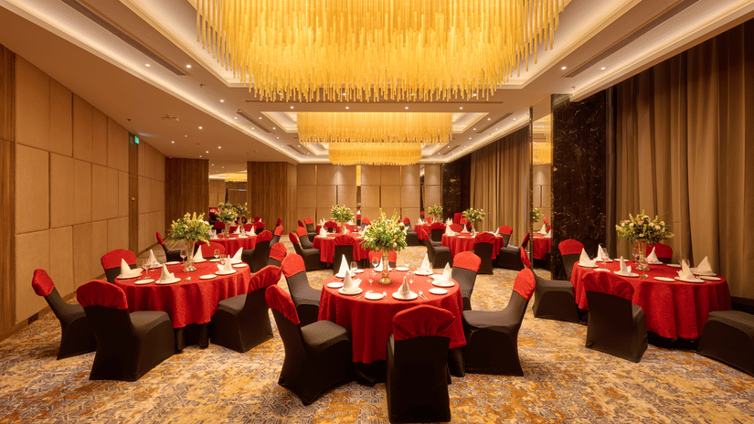 A large banquet hall at KPG Sarovar Portico, Raj Nagar Extension, Ghaziabad featuring round dining tables, chairs, chandeliers, and carpeted flooring.