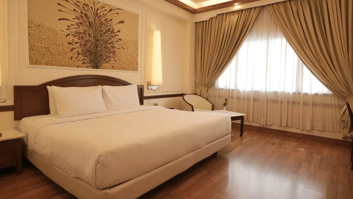 A well-lit bedroom with a king size bed, wooden flooring, curtains, and a seating area, reflecting comfortable rooms in Jaipur - Clarks Amer, Jaipur