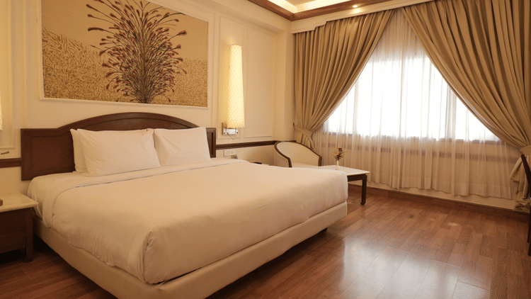 A well-lit bedroom with a king size bed, wooden flooring, curtains, and a seating area, reflecting comfortable rooms in Jaipur - Clarks Amer, Jaipur
