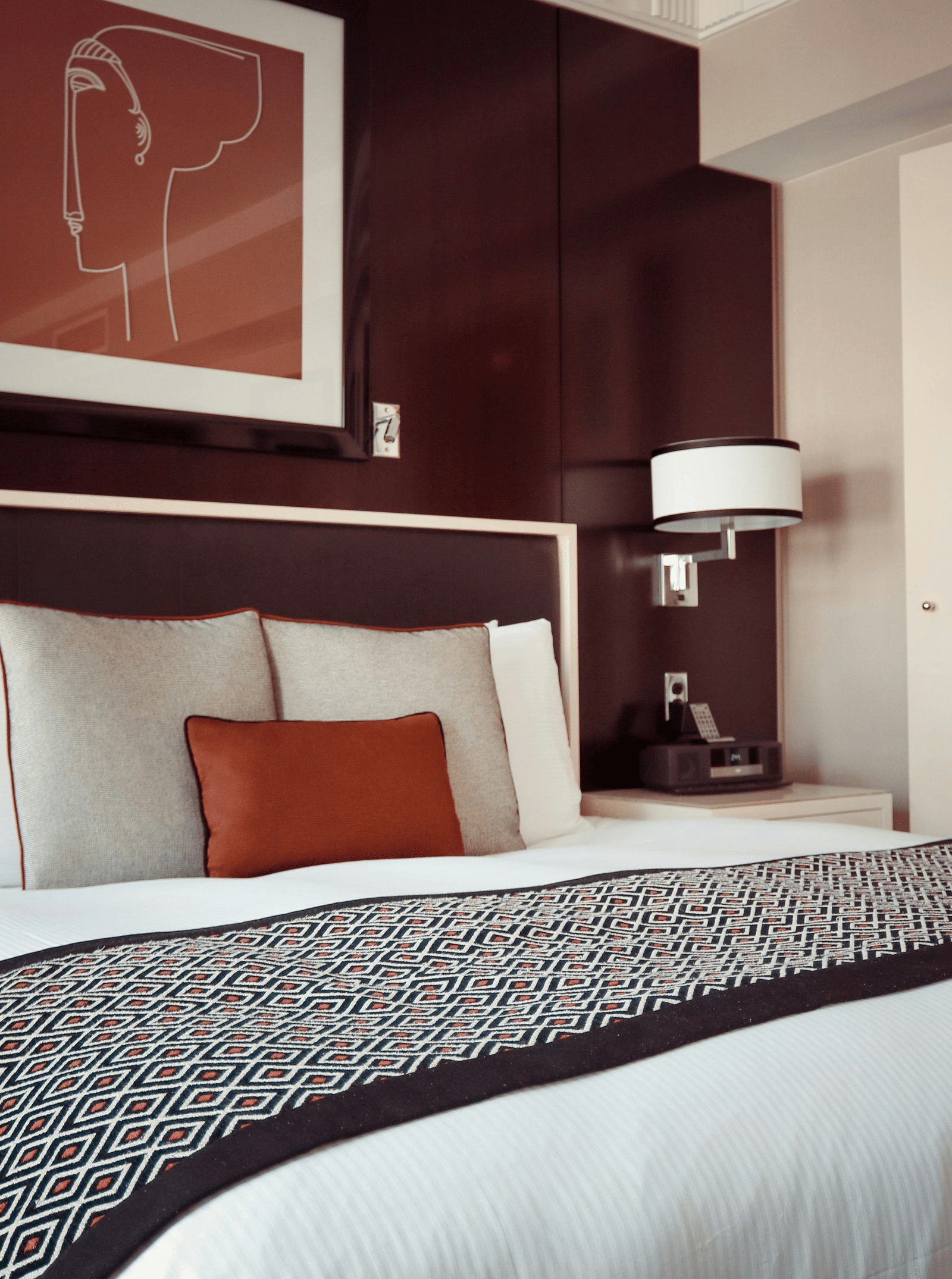 A luxurious hotel bedroom with a large bed, dark wood panelled walls, and an adjoining en-suite bathroom visible through glass doors.