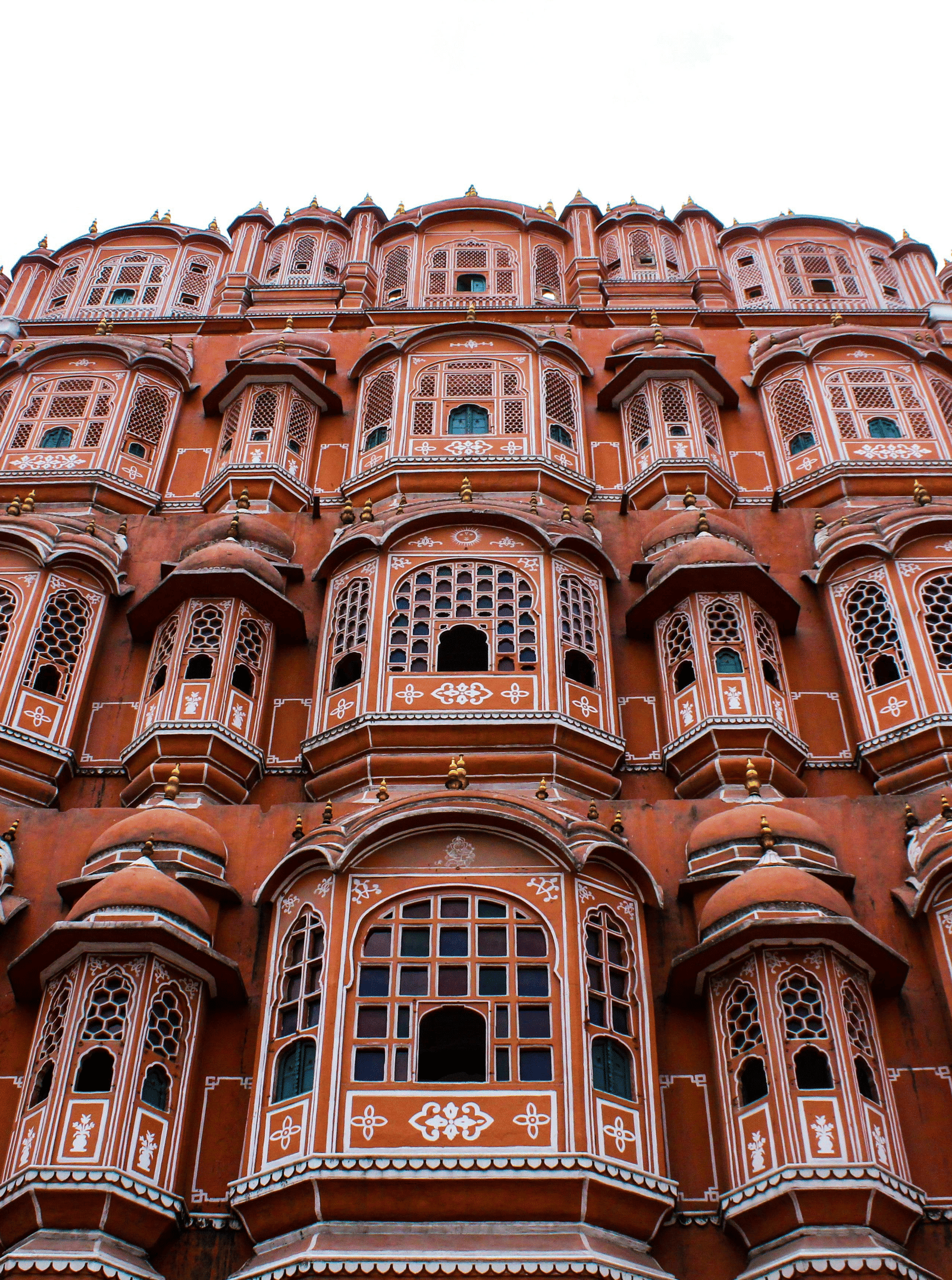 A low-angle view of the Hawa Mahal, Jaipur, showing its distinctive 5-storey pink sandstone façade with many windows.