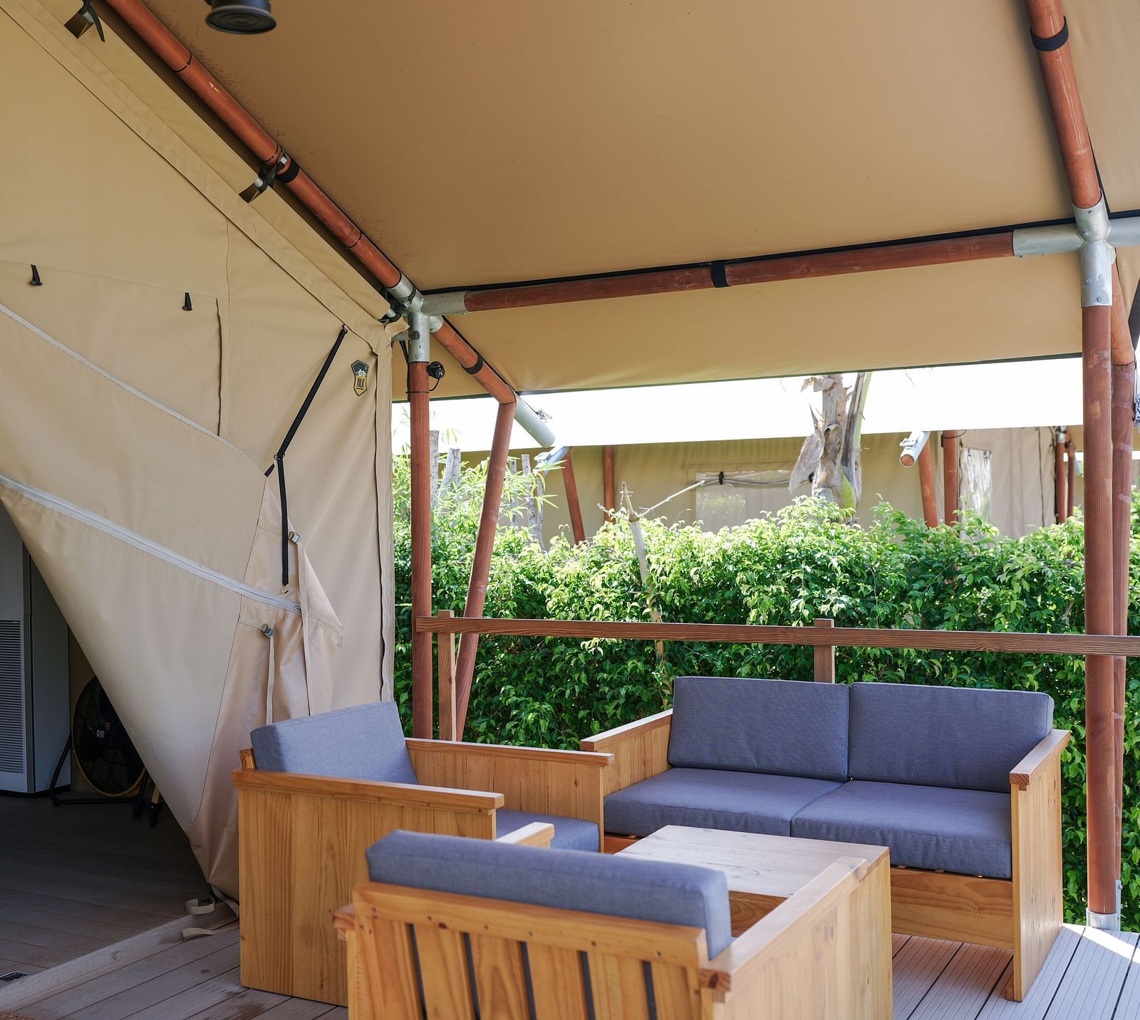  A spacious interior view of the Mindful Tent at WoCAL Retreat Ke Ga, showing a seating area with a sofa, a wooden dining table, chairs, and shelves.