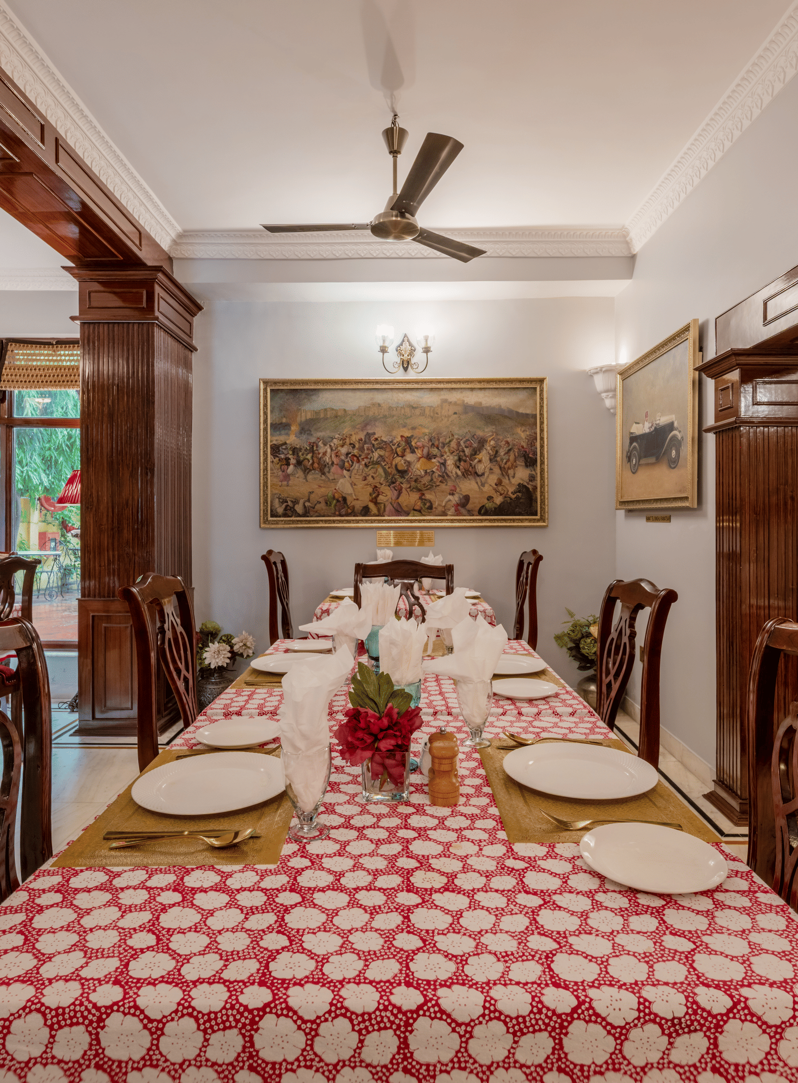 Traditional dining hall with red checkered tablecloths, wooden pillars, and chandelier at Dera Rawatsar, Jaipur.