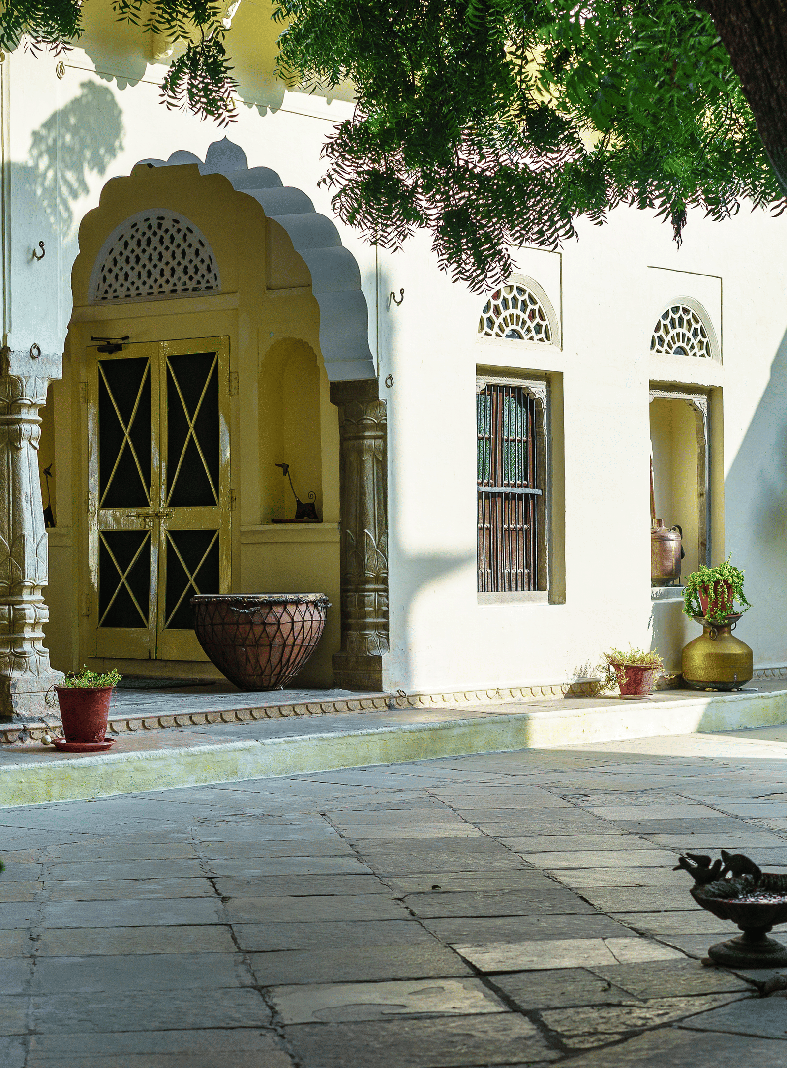 A serene courtyard at Fort Barli, with arched doorways and a large tree, captures the fort's tranquil atmosphere.