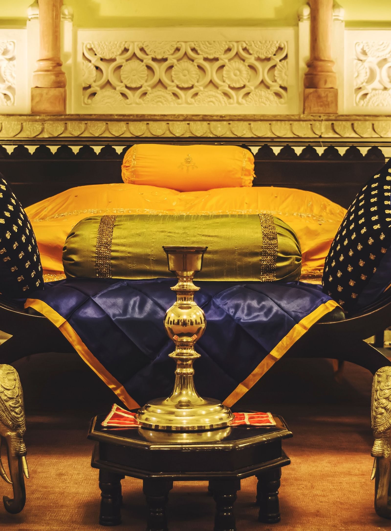 A luxuriously decorated bed at Umaid Vilas Jaipur with ornate elephant sculptures at its foot, showcasing traditional Indian design.