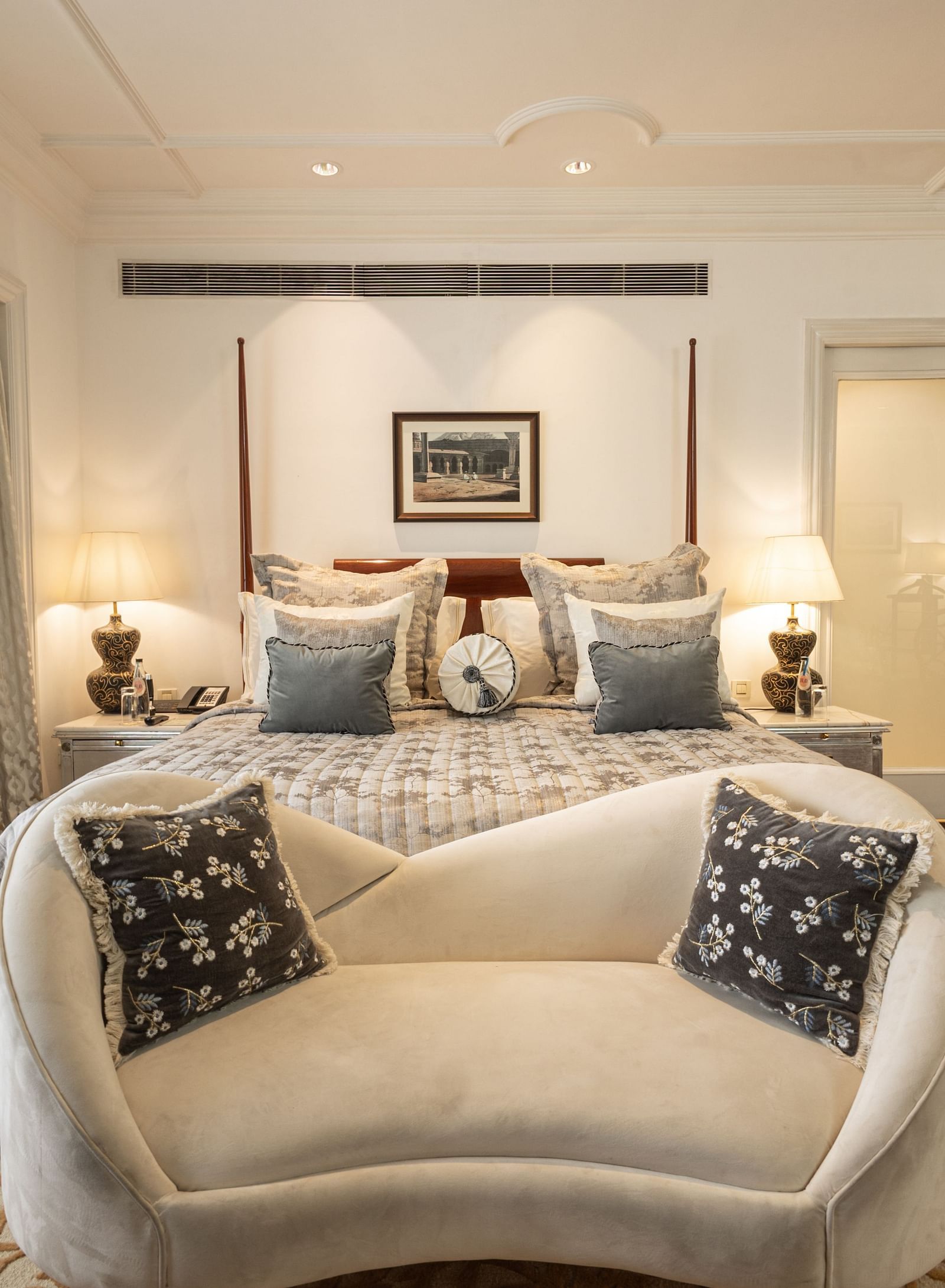 image of plush king size bed along with a white couch in front of it at our viceroy house estate suite - Two chairs, accompanied by a small coffee table, are placed in the middle of the room at The Claridges New Delhi. 