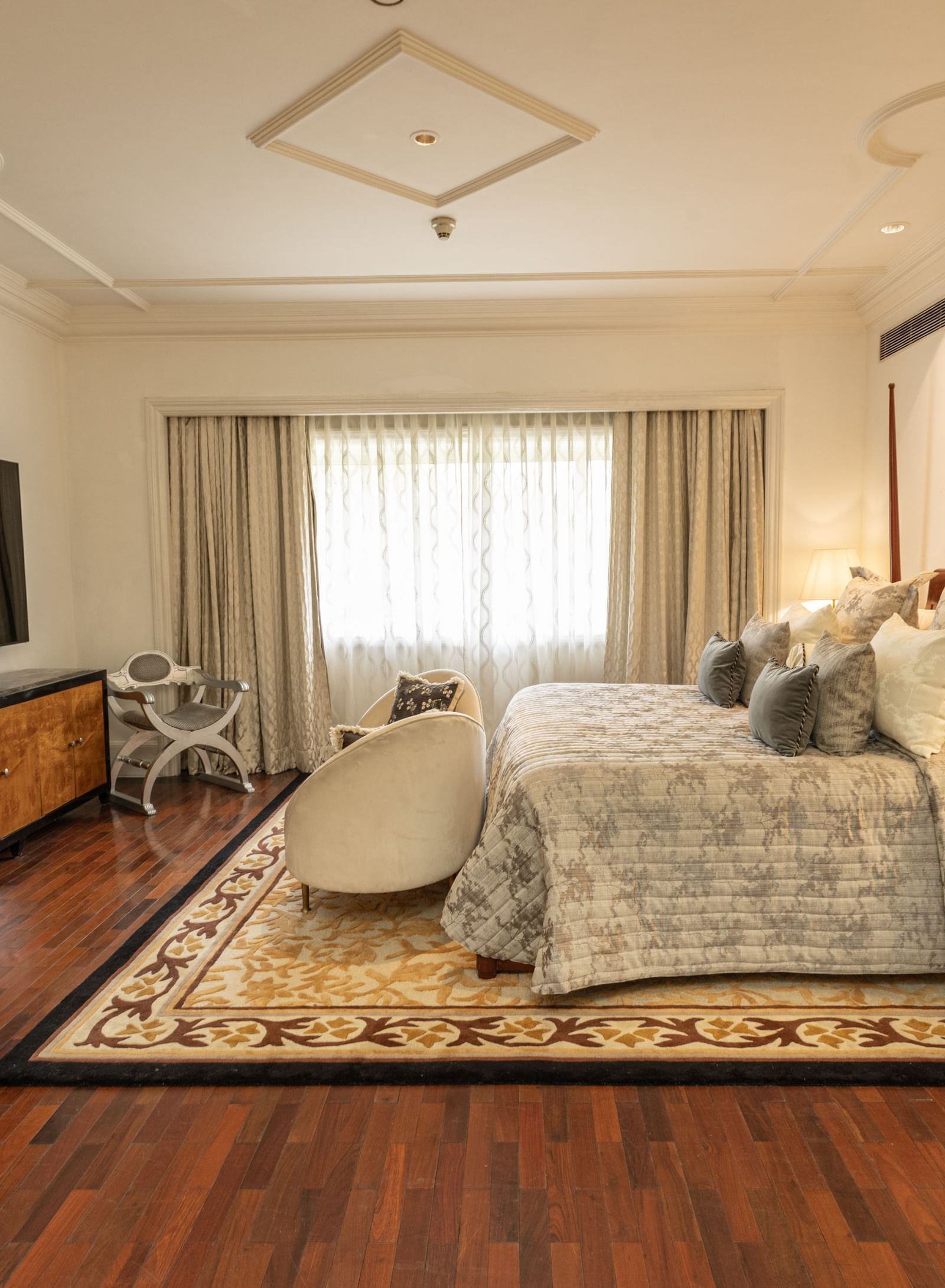 The Claridges New Delhi bright bedroom is furnished with two double beds, dark wood floors, and a patterned rug.