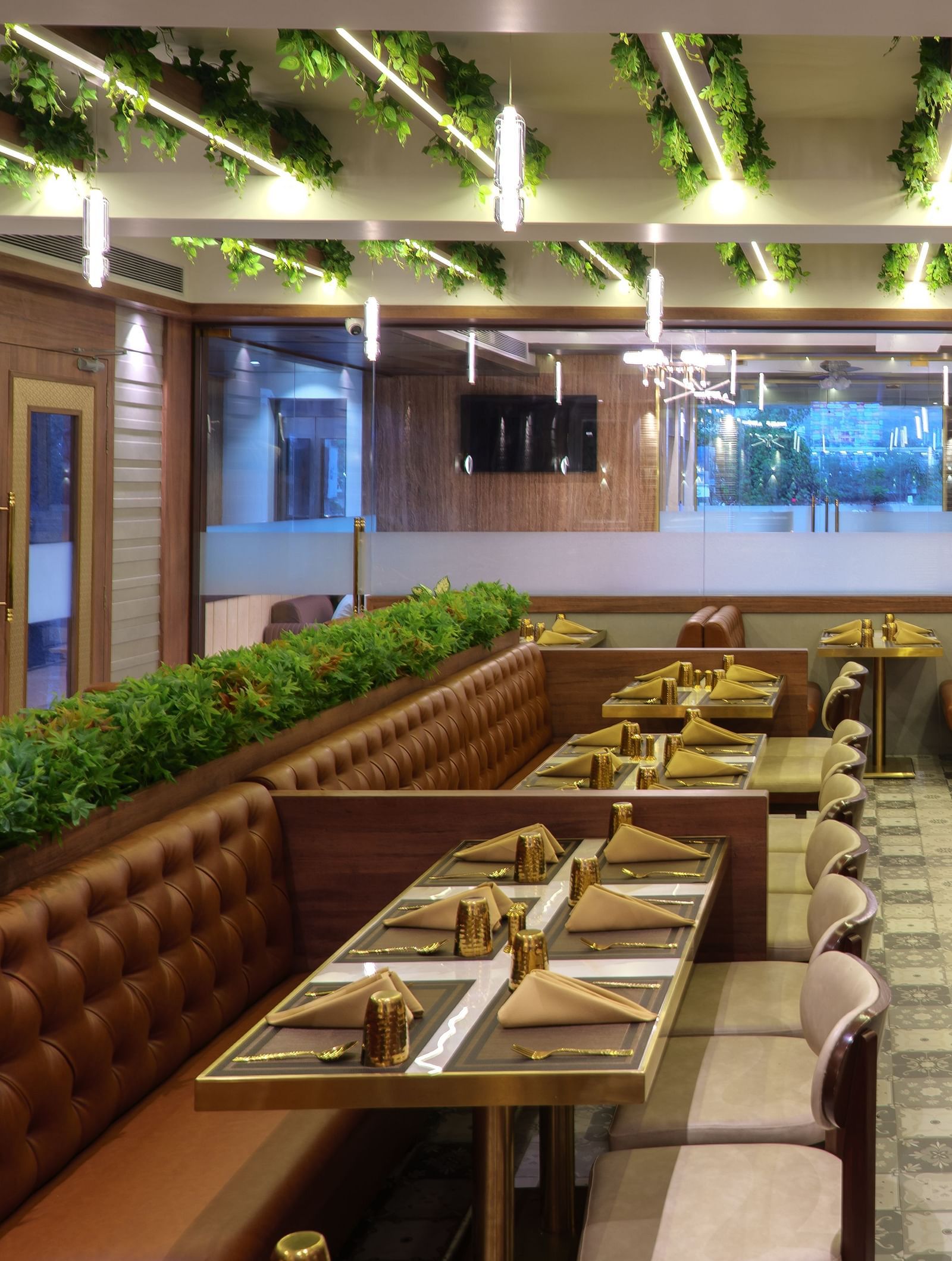 A spacious restaurant with numerous wooden tables and chairs, featuring bright overhead lighting and some greenery - Melior Inn
