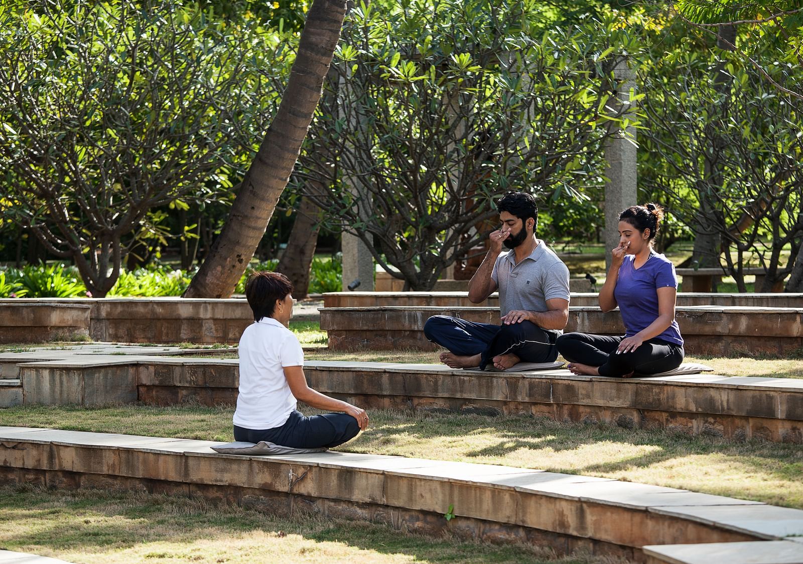 People sitting on steps outdoors, trees, performing yoga - Shreyas Retreat
