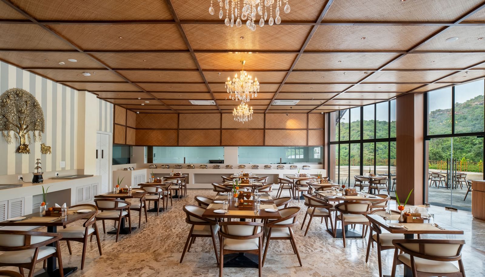 A well-lit restaurant interior at Osian Valley Resort & Spa with multiple square wooden tables and chairs arranged on a patterned floor. 